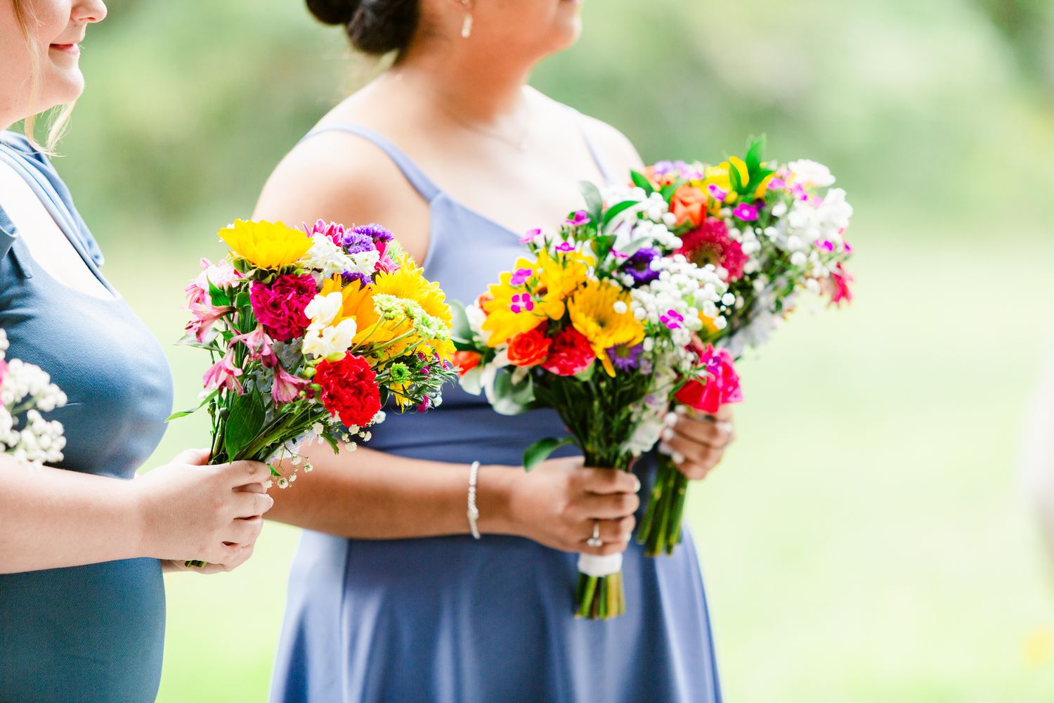 A row of colorful wedding bouquets with vibrant wildflowers and sunflowers held against blue bridesmaid dresses.