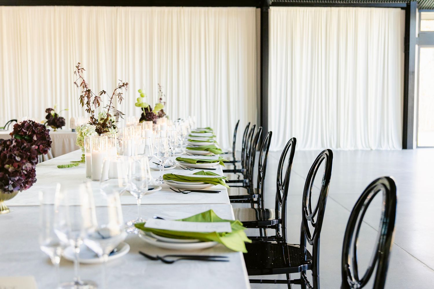 Elegant white dining tables set with green placemats and black chairs in a modern restaurant interior.