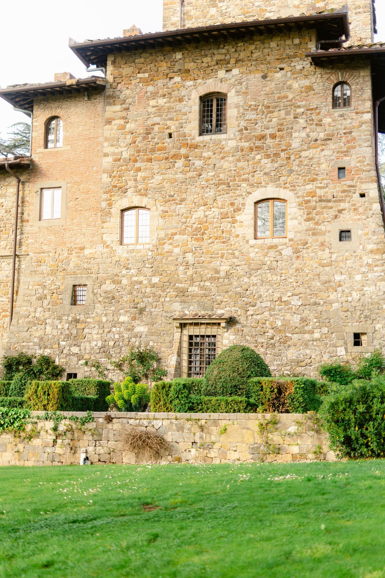 Ancient stone castle wall with arched windows and manicured green lawn in foreground.
