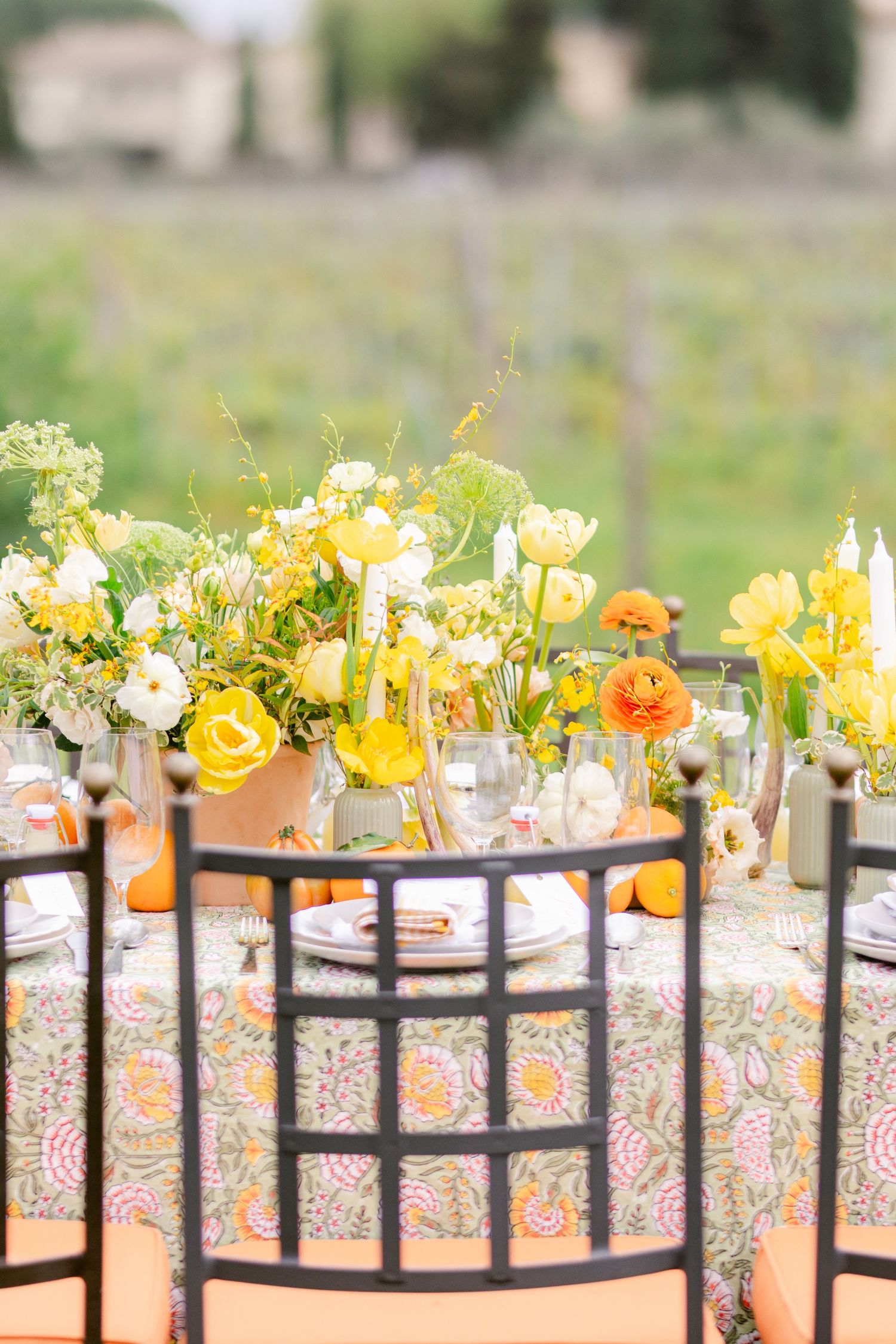 Yellow and orange spring flowers arranged in glass vases on black metal railings create an elegant outdoor display.