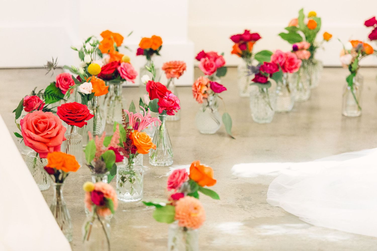 Vibrant red and orange roses displayed in small glass vases along a table setting.