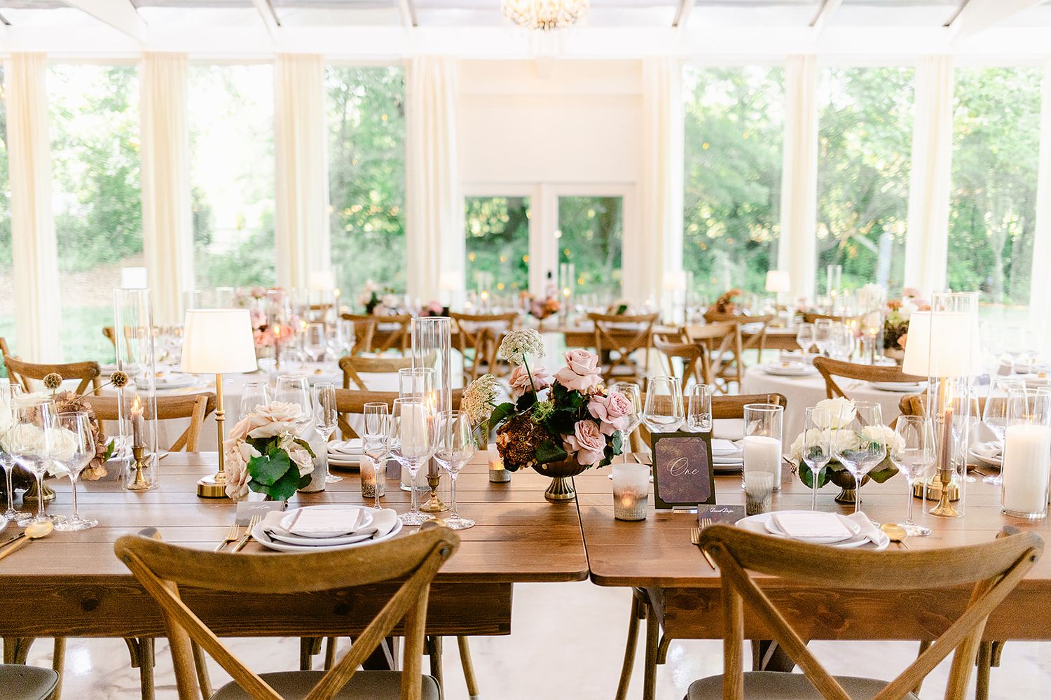 Elegant wedding reception tables set with wooden chairs and floral centerpieces under a white tent pavilion.