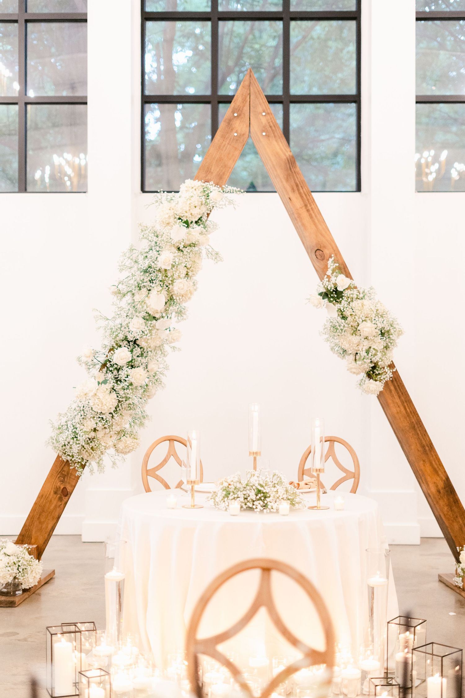 Elegant wedding reception venue with wooden geometric arches and white floral arrangements.