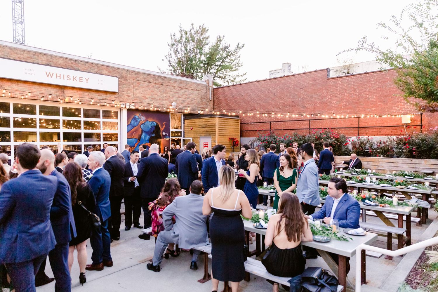 Reception guests mingle in an outdoor brick courtyard with tables and decorations.