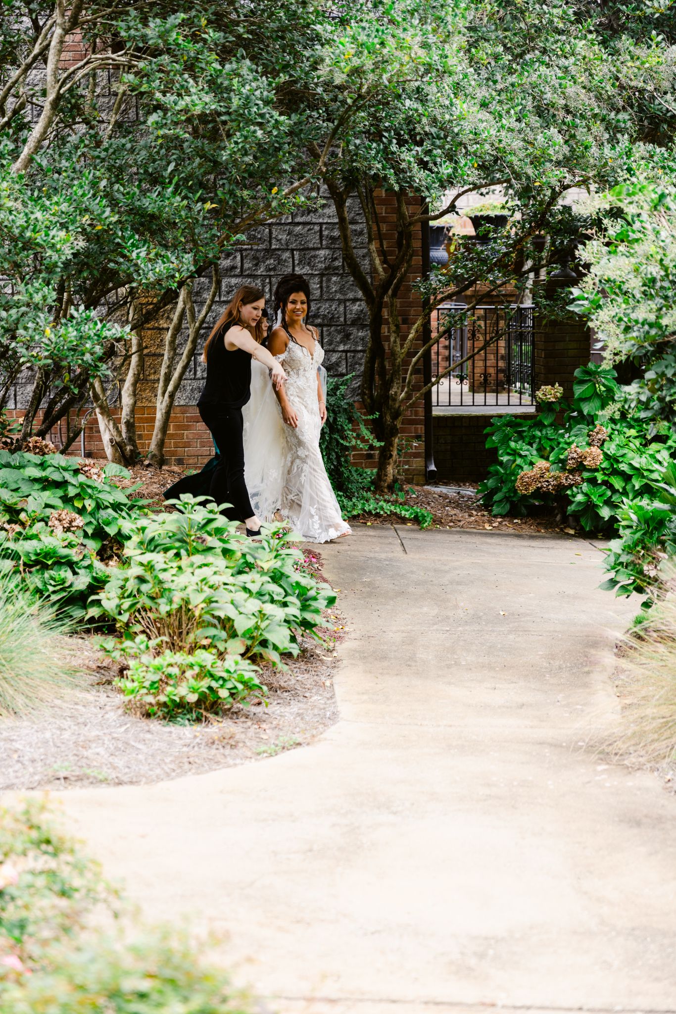 A couple shares a romantic moment in a lush garden courtyard surrounded by green foliage and brick walls.