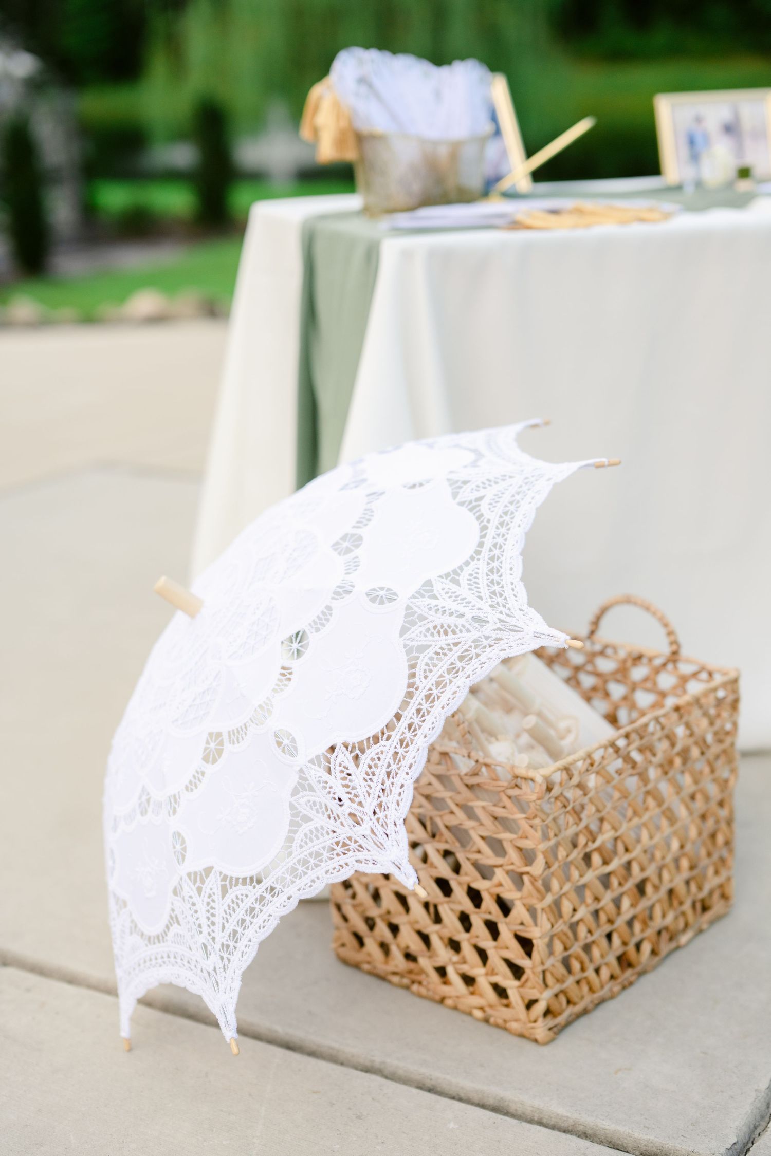 A delicate white lace parasol rests beside a woven basket on a light stone surface.