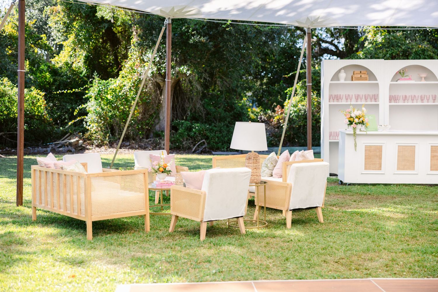 Outdoor lounge area setup with white furniture and canopy for a garden wedding reception.