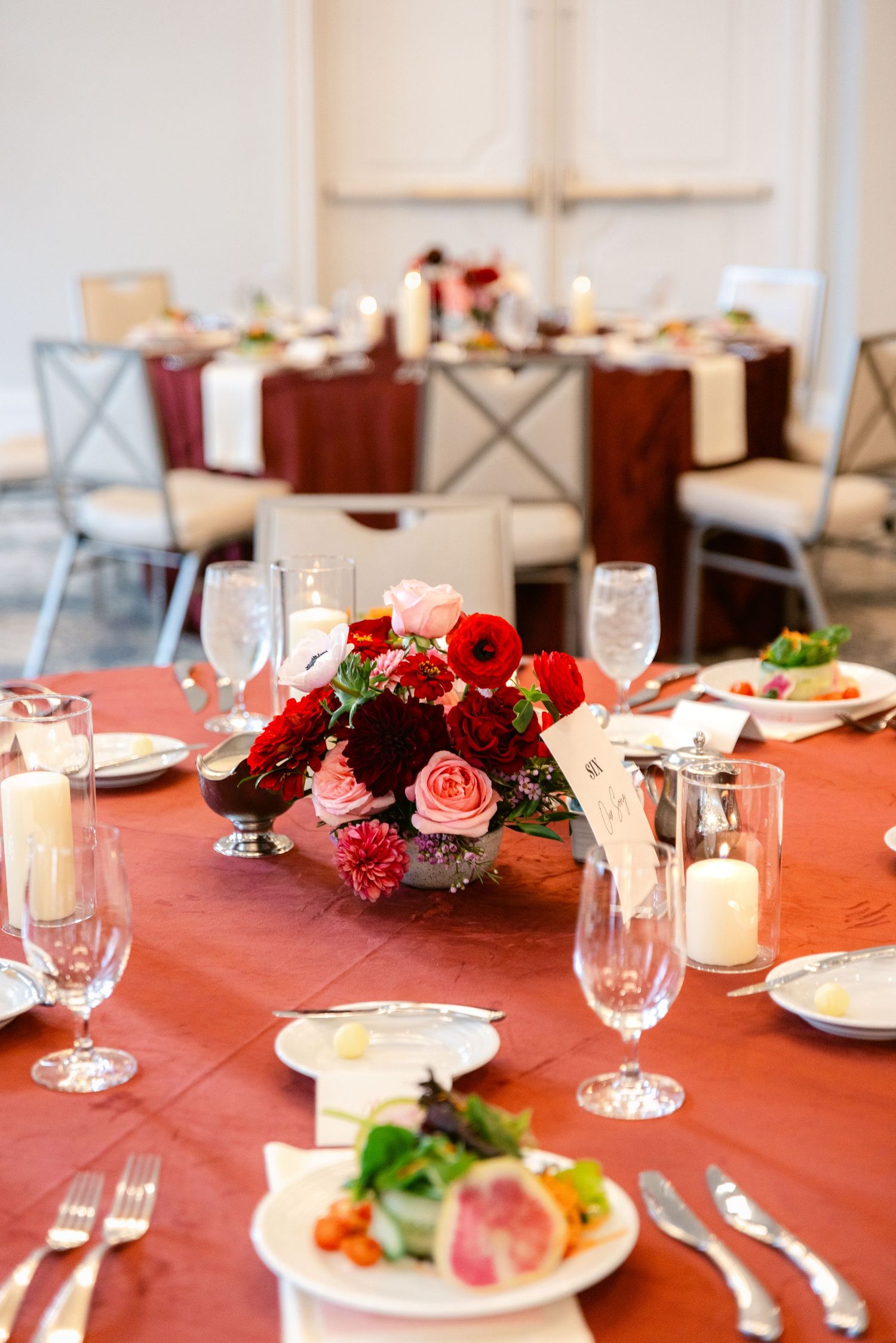 Elegant table settings with coral linens, wine glasses, and pink floral centerpieces create a romantic dining atmosphere.