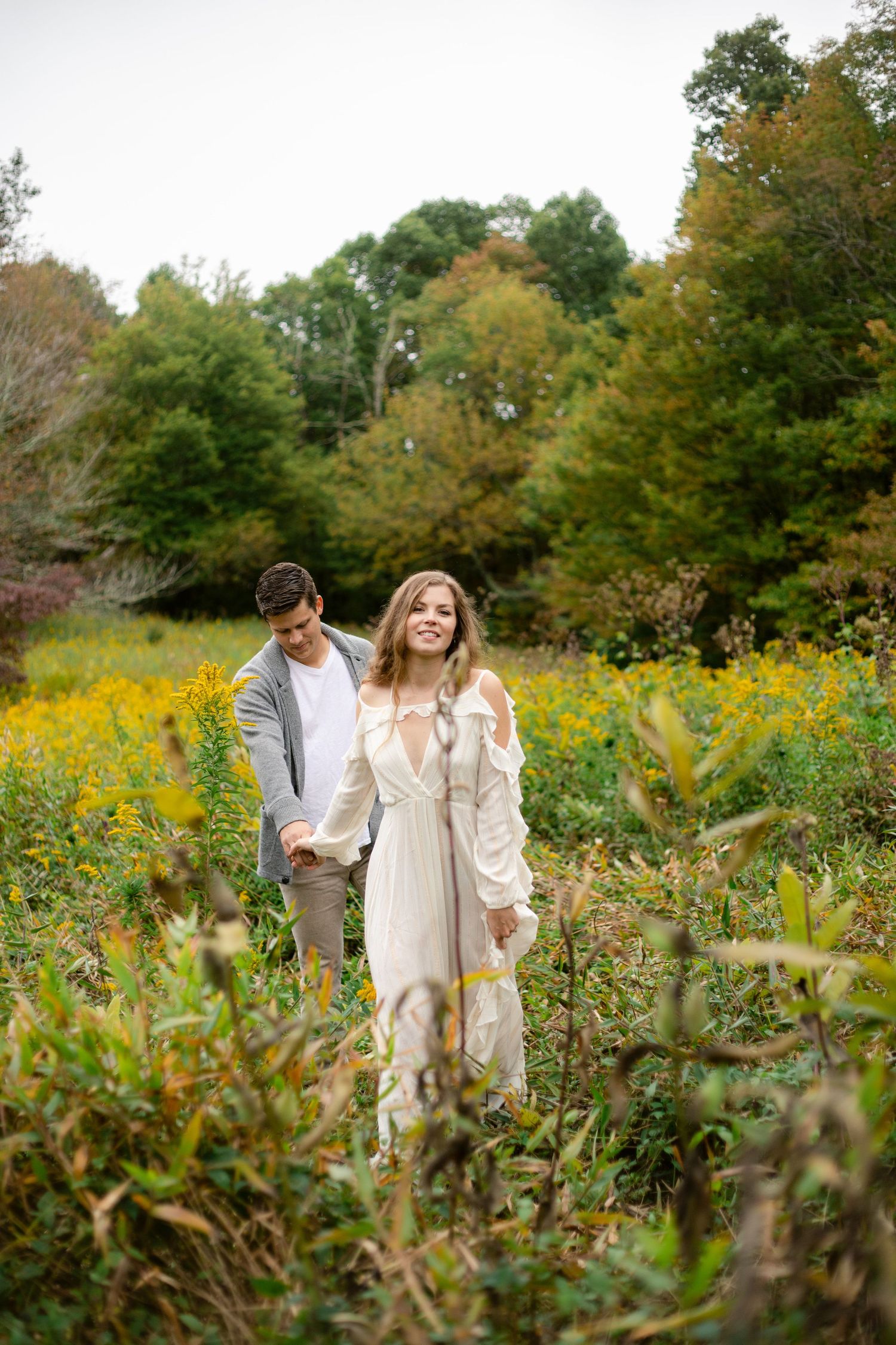 A romantic engagement photo in a meadow filled with yellow wildflowers and fall foliage.