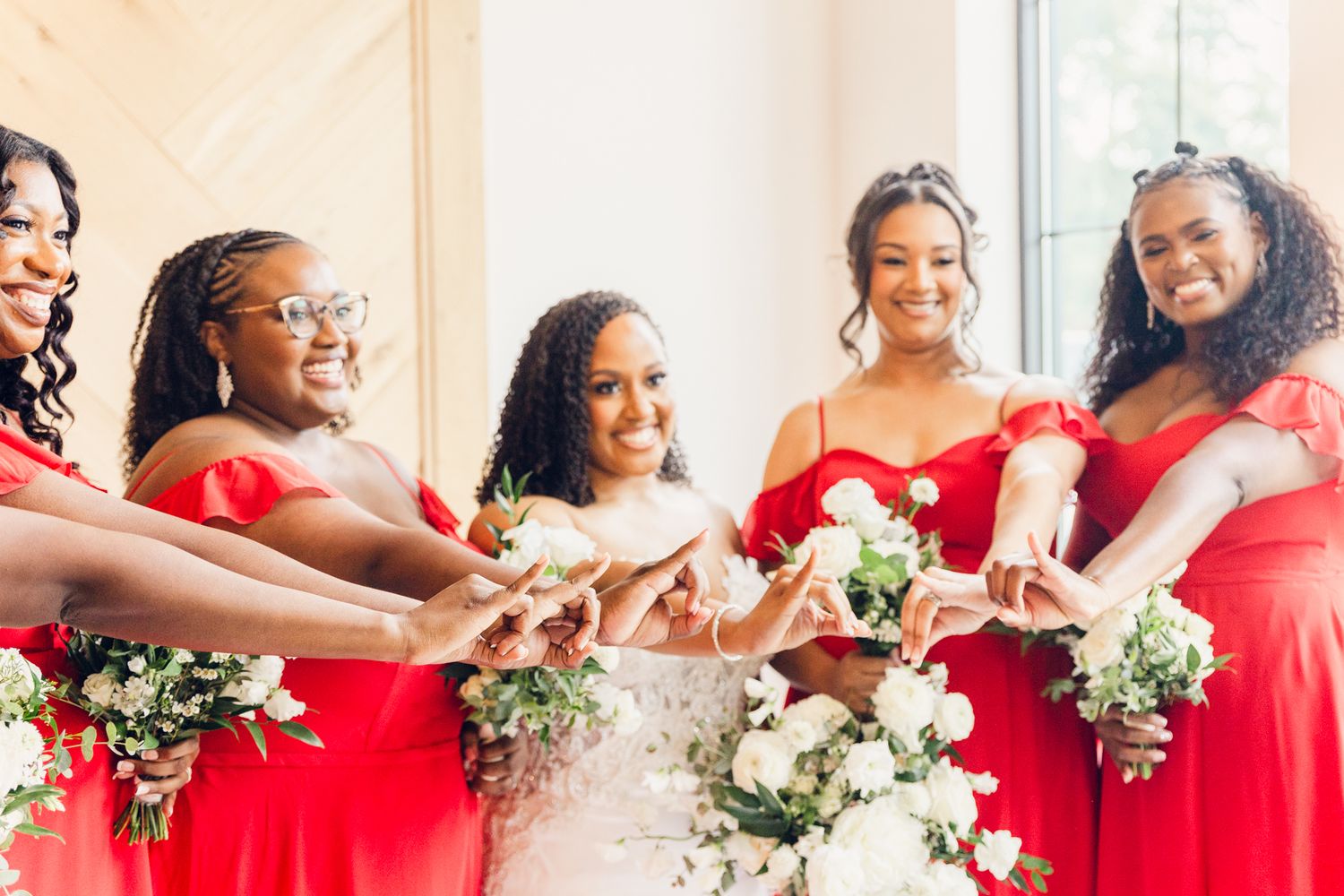 Bridesmaids in vibrant red dresses pose together while holding white floral bouquets at a wedding.