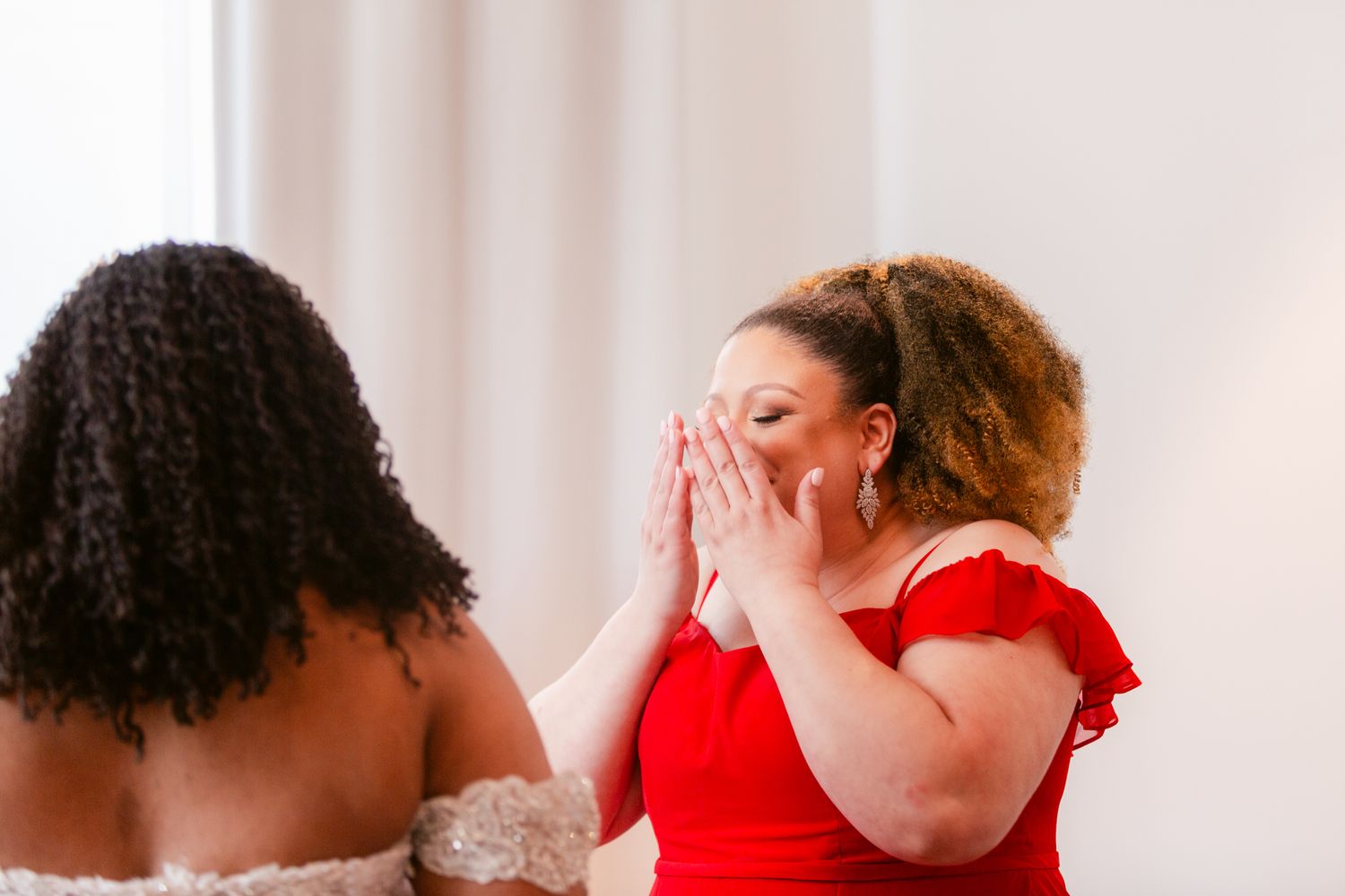 Wedding party members in red dresses and black suits share emotional embraces during celebration.