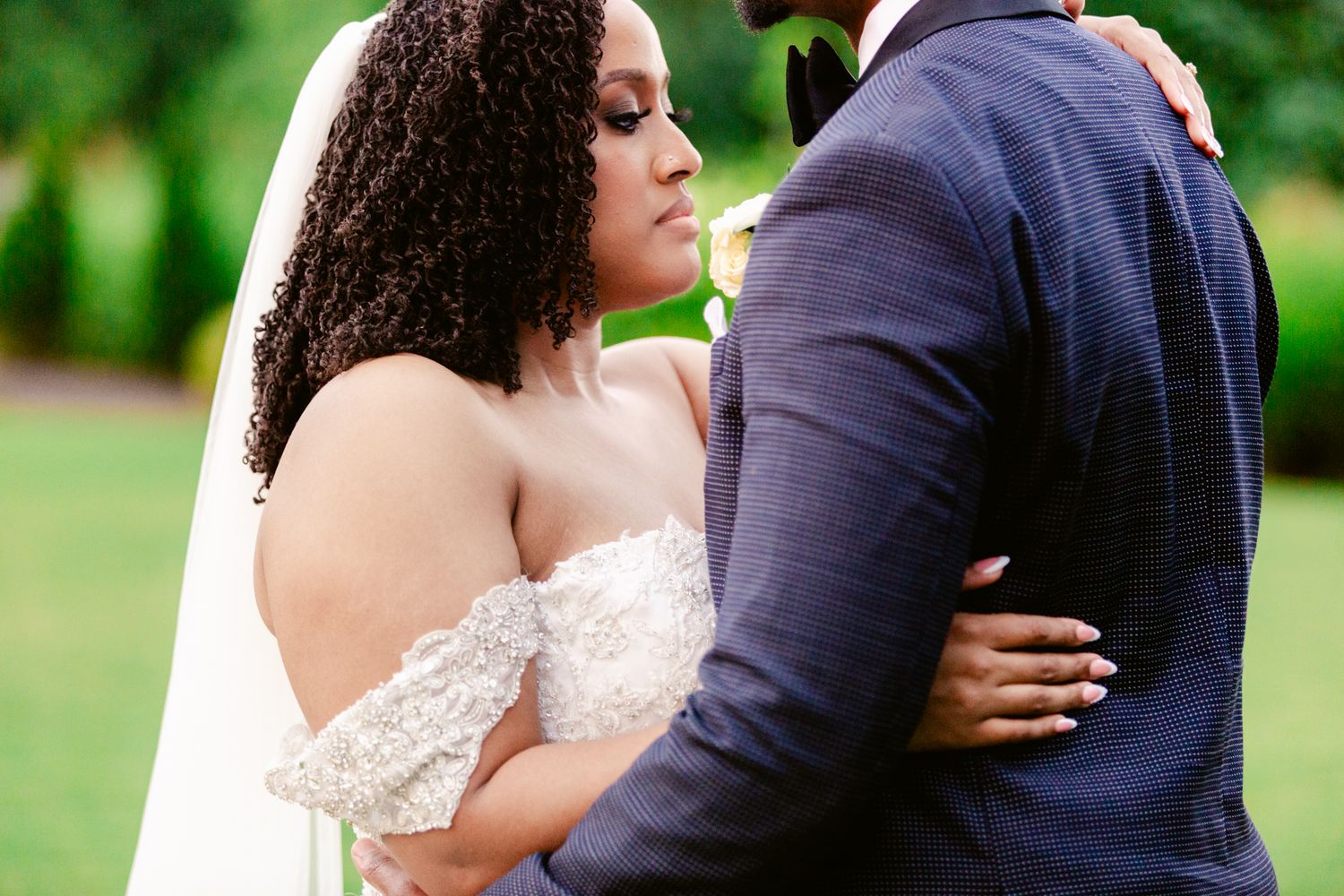 A couple embraces during an outdoor wedding photoshoot in a lush green garden setting.