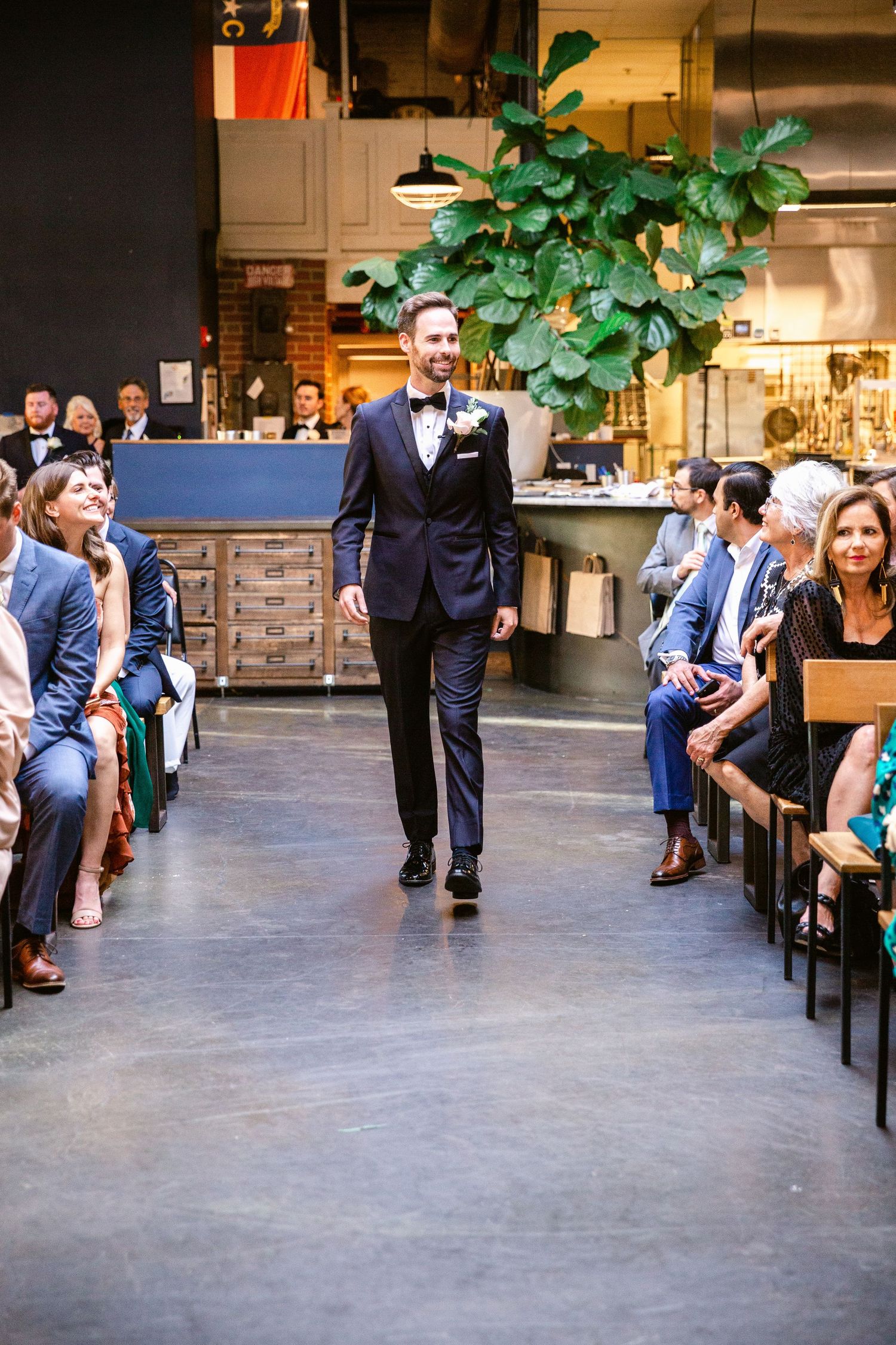 Wedding guests dance and socialize in an industrial-chic venue with concrete floors and potted plants.
