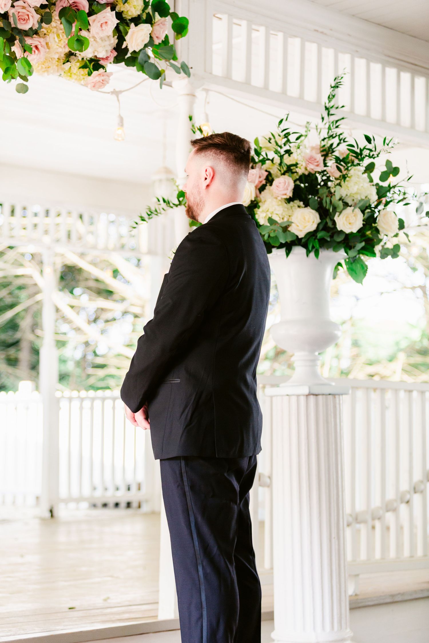 Couple sharing an intimate embrace on a white gazebo decorated with pink roses and greenery.