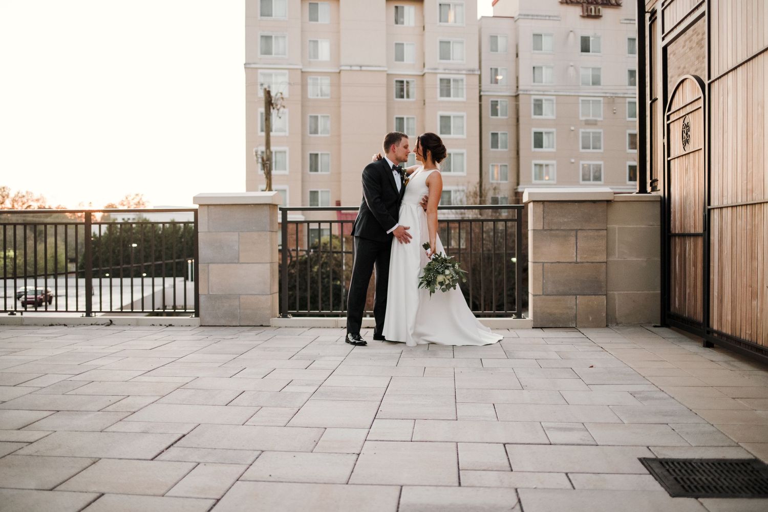 Wedding couple shares romantic moment on urban rooftop terrace with modern building backdrop.