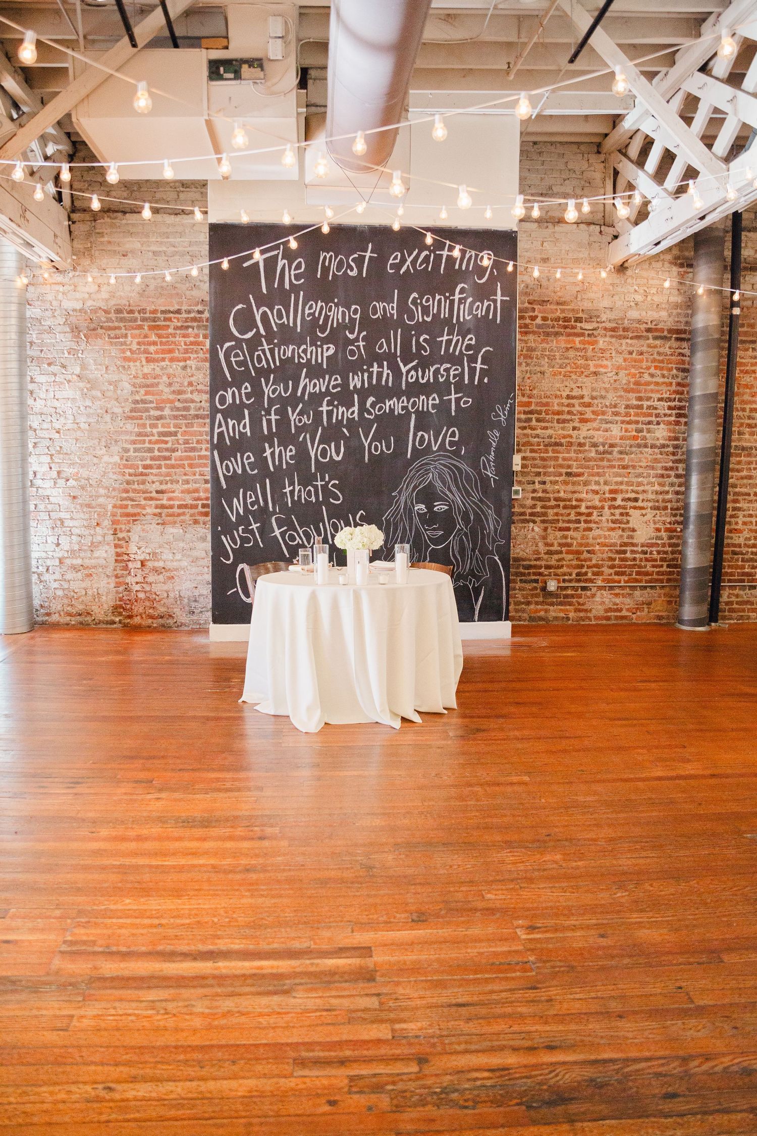 Wedding venue space with inspirational chalkboard quote, string lights and hardwood floors.