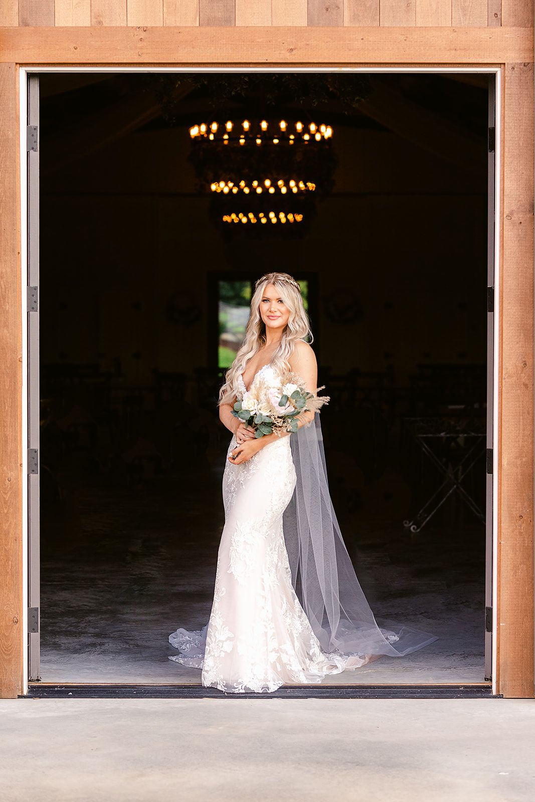 An elegant wedding dress silhouette framed in a doorway with chandeliers above.