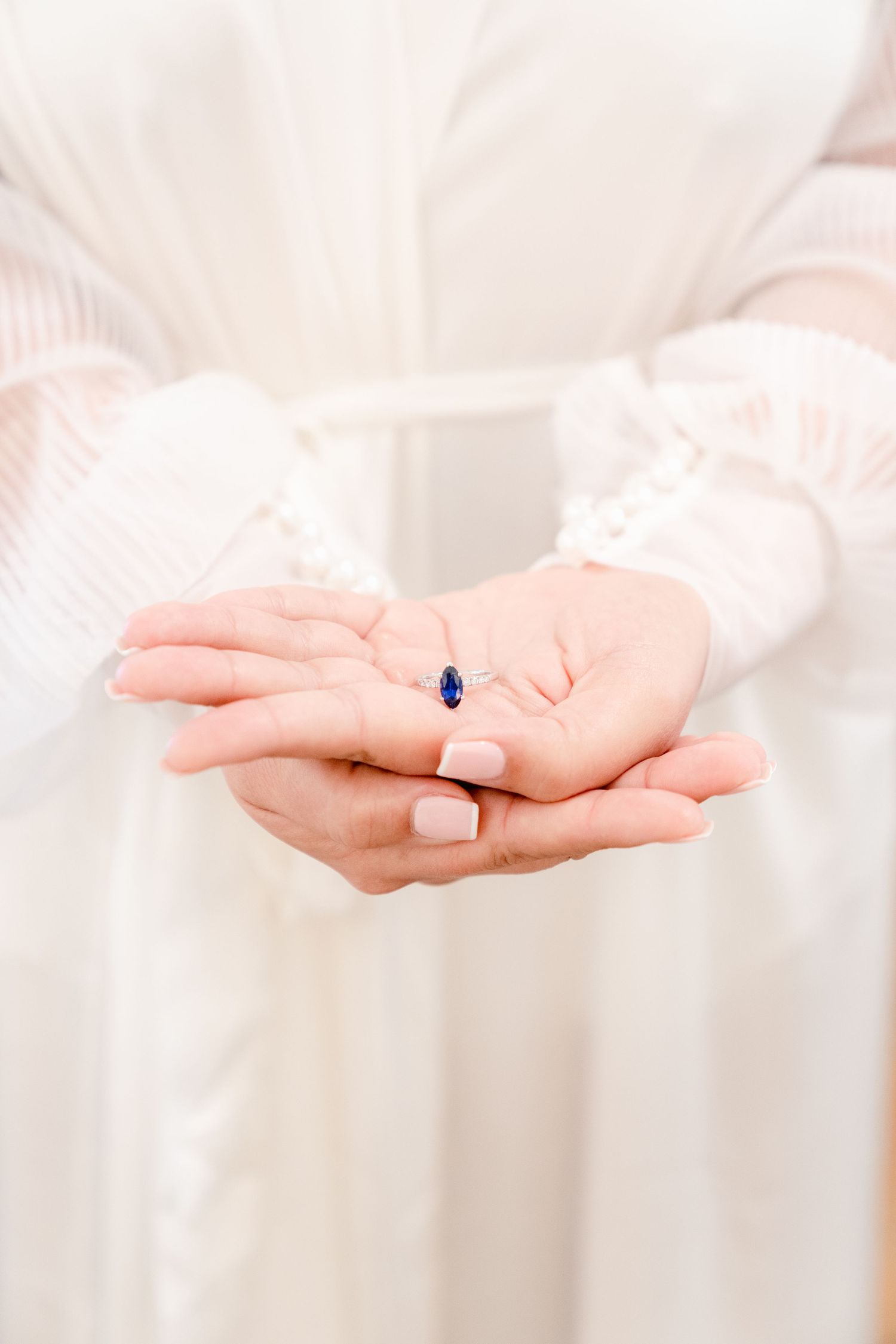 Elegant blue gemstone ring presented in open palms against white fabric background.