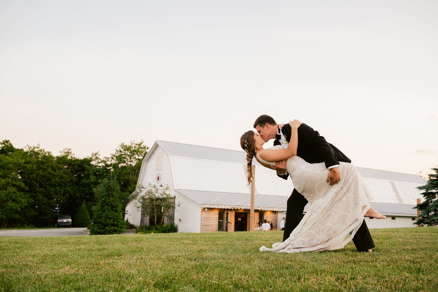 Romantic dip pose with white barn in background during sunset wedding photoshoot.