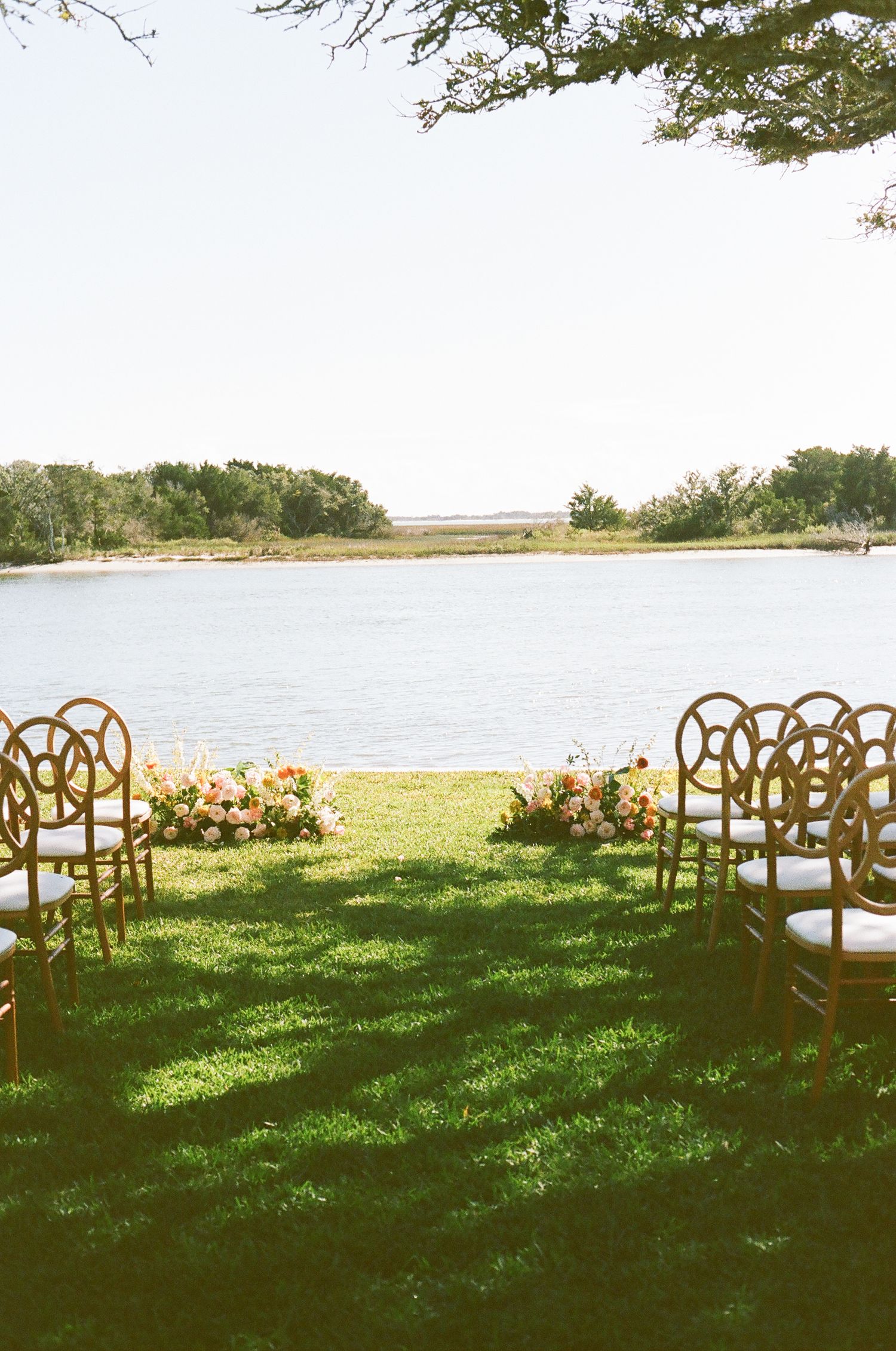 Rustic wooden cross-back chairs arranged for an outdoor waterfront wedding ceremony.