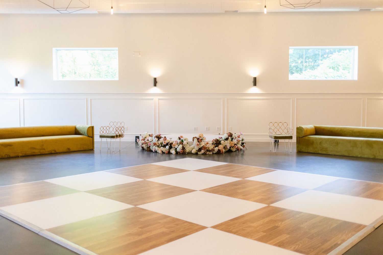 Large empty dance studio with checkered wood flooring and mirrored walls illuminated by natural light.