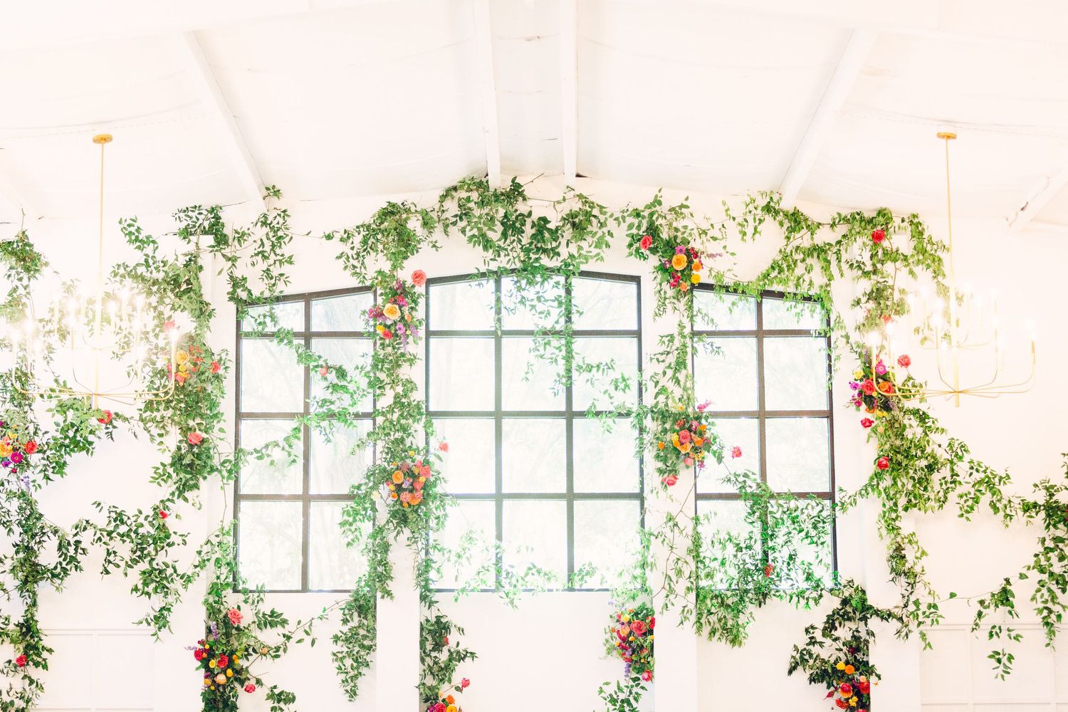 A bright indoor venue decorated with climbing greenery and windows creating a romantic wedding atmosphere.