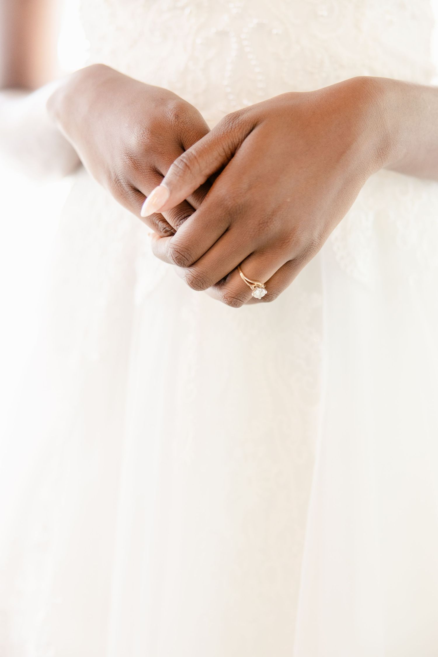 Close-up of hands wearing an elegant diamond engagement ring against a white background.