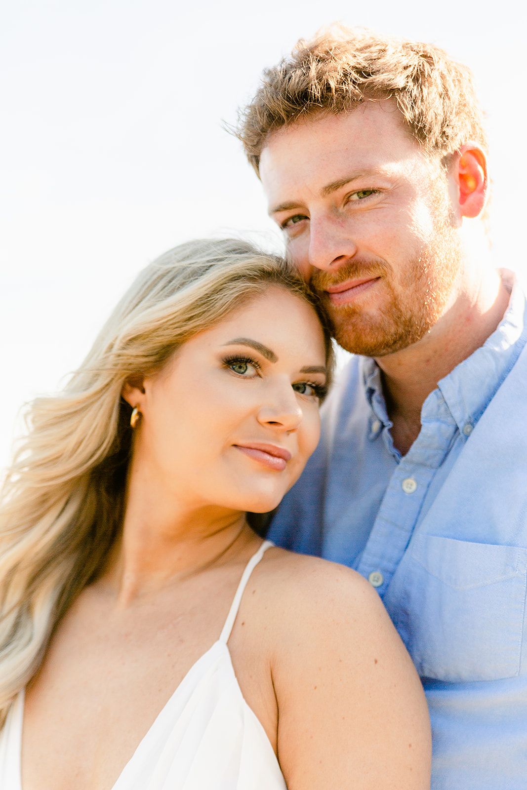 Romantic couple in light blue shirt and white dress share intimate close-up moments against bright background.