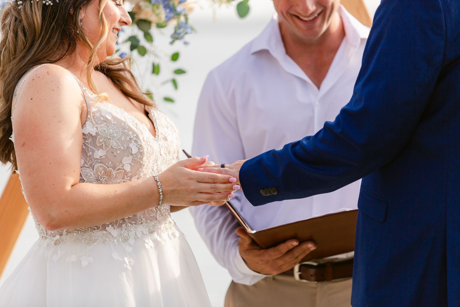 Bride and groom exchange rings during an outdoor wedding ceremony surrounded by greenery and natural light.