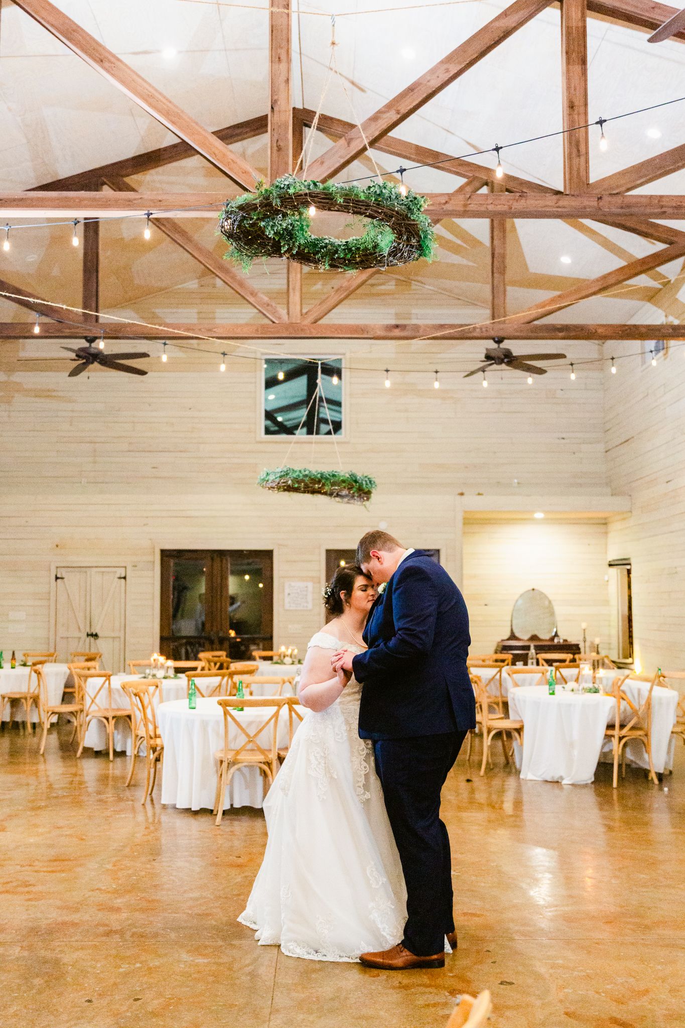 Elegant wedding reception venue with exposed wooden beams, white decor, and romantic lighting setup.