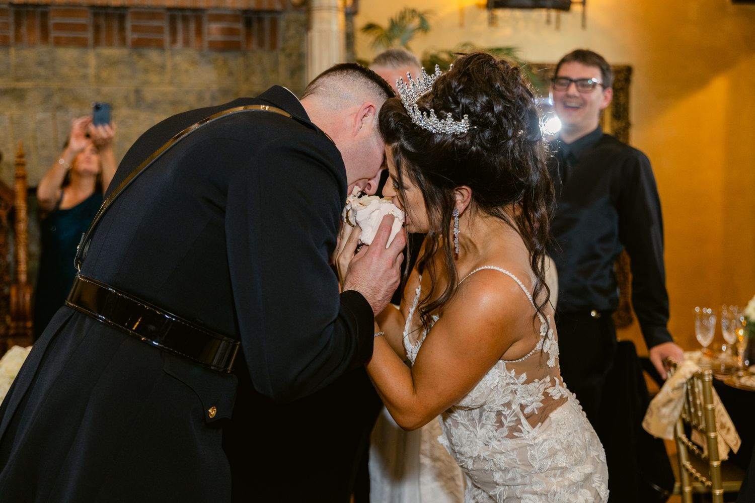 A couple shares an intimate kiss during their wedding reception while guests look on in the background.