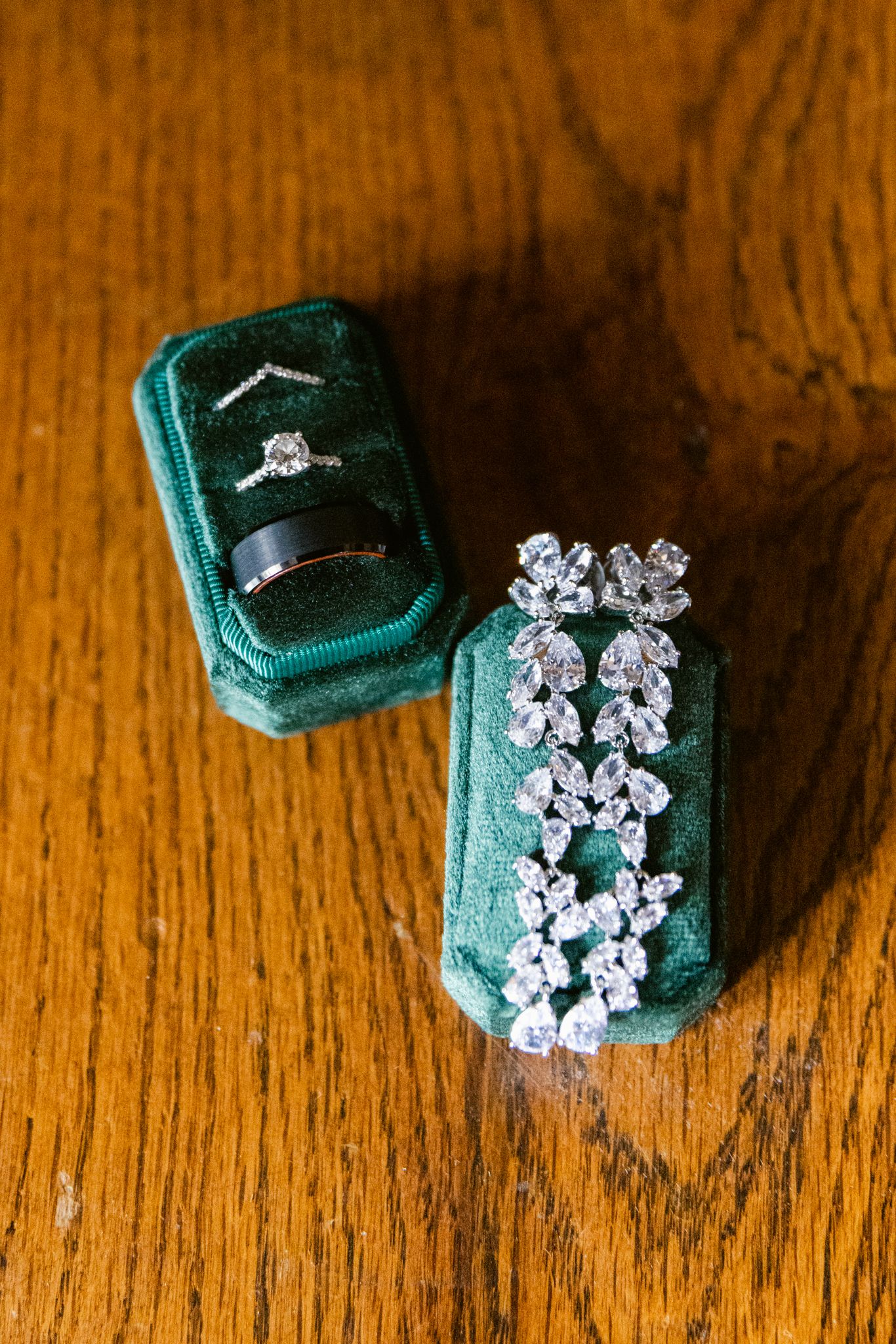 Four emerald green velvet ring boxes with diamond jewelry displayed on a wooden surface.