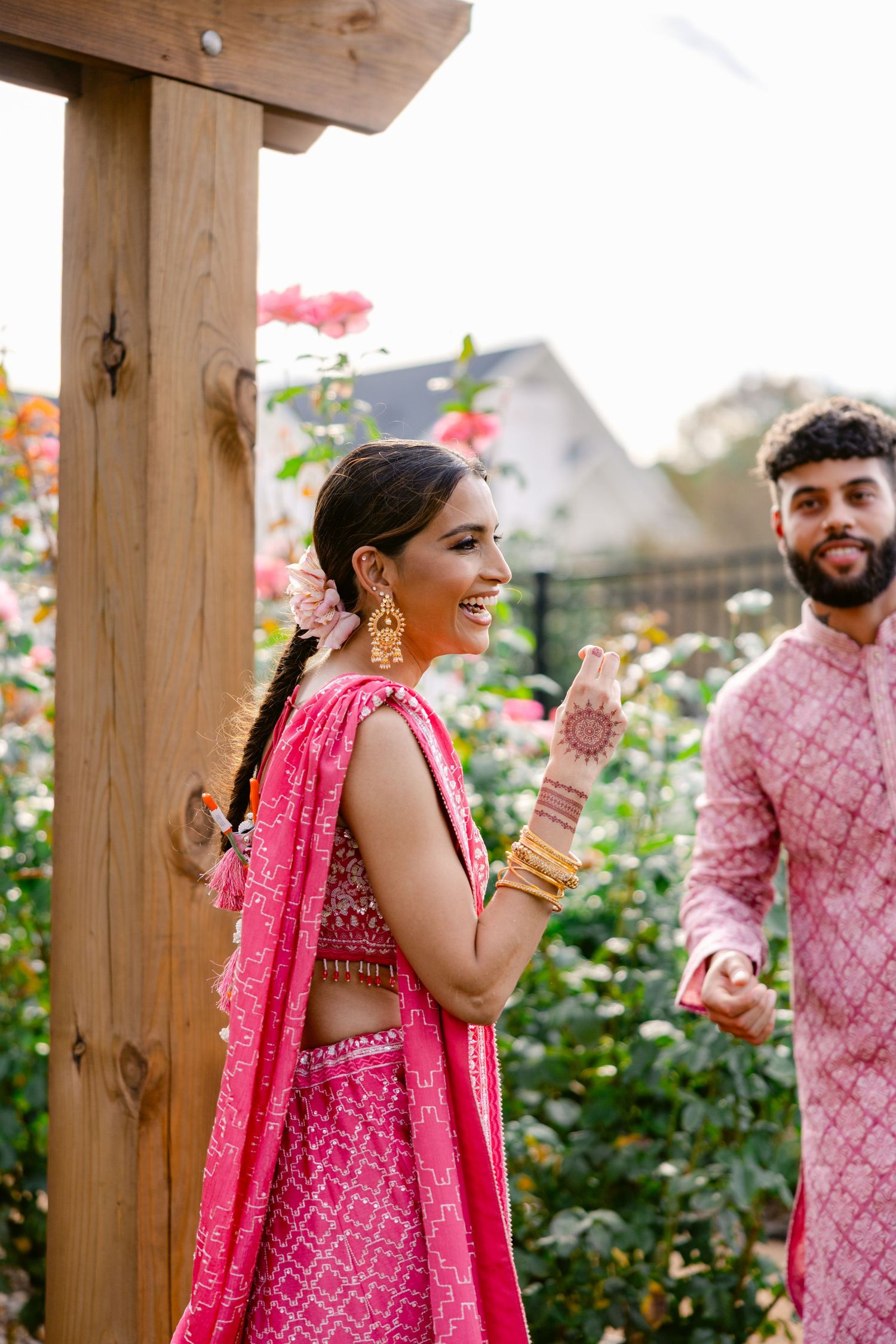 Couple in matching pink Indian outfits posing playfully in a garden setting.