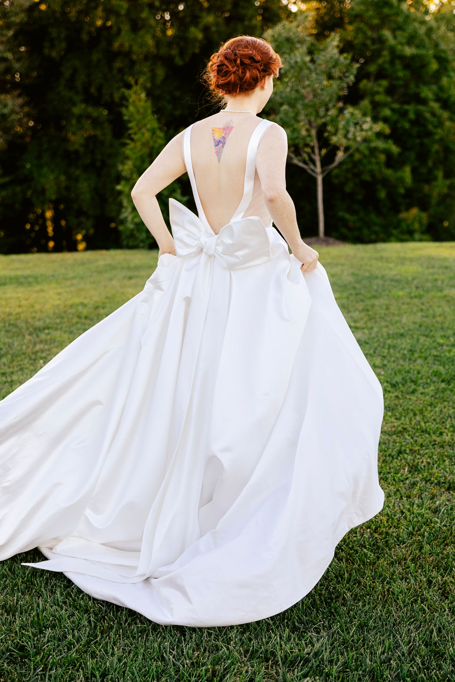 Flowing white wedding dress twirls on green grass during a sunset photoshoot.