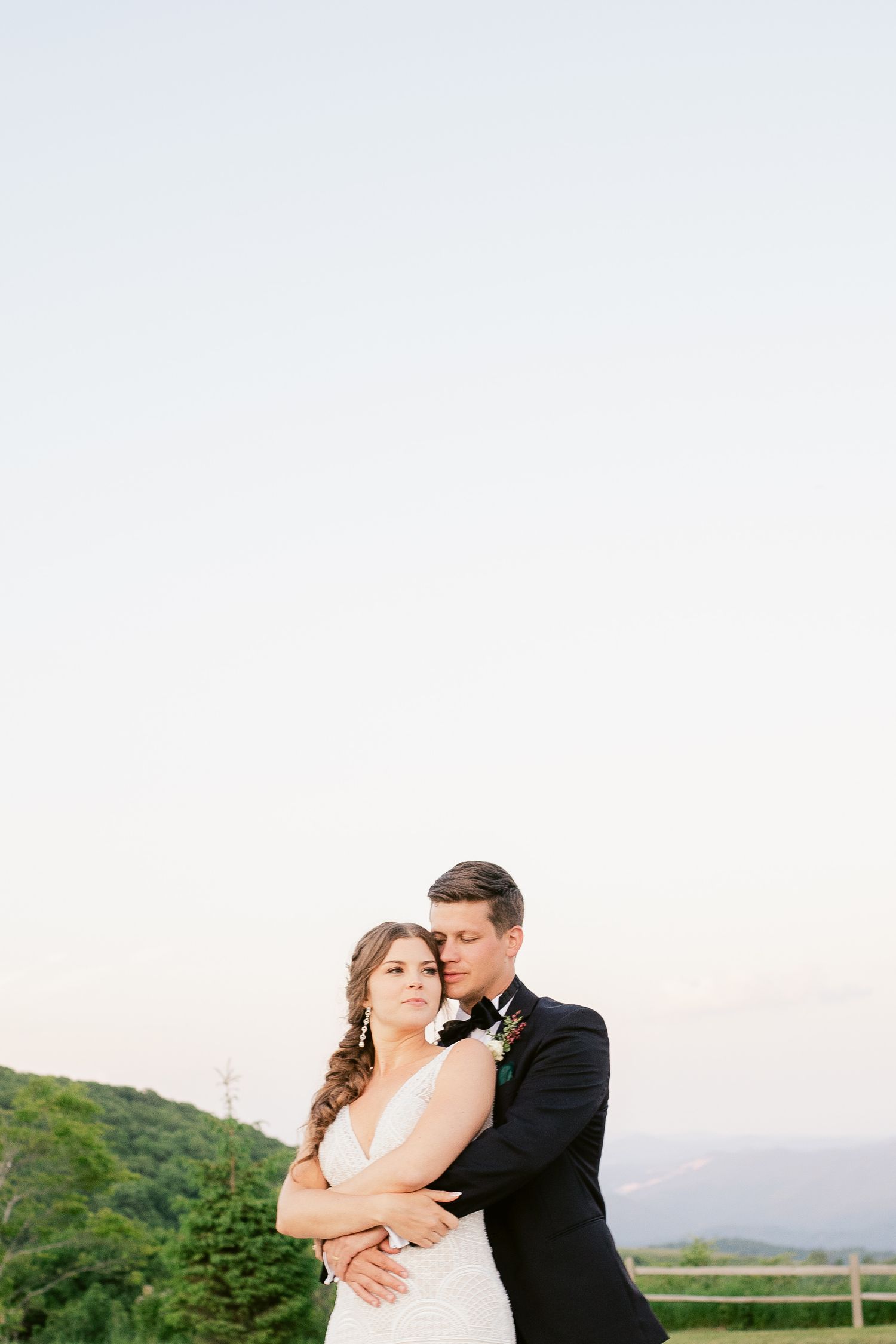 A couple embraces against a scenic mountain backdrop at sunset during their wedding celebration.