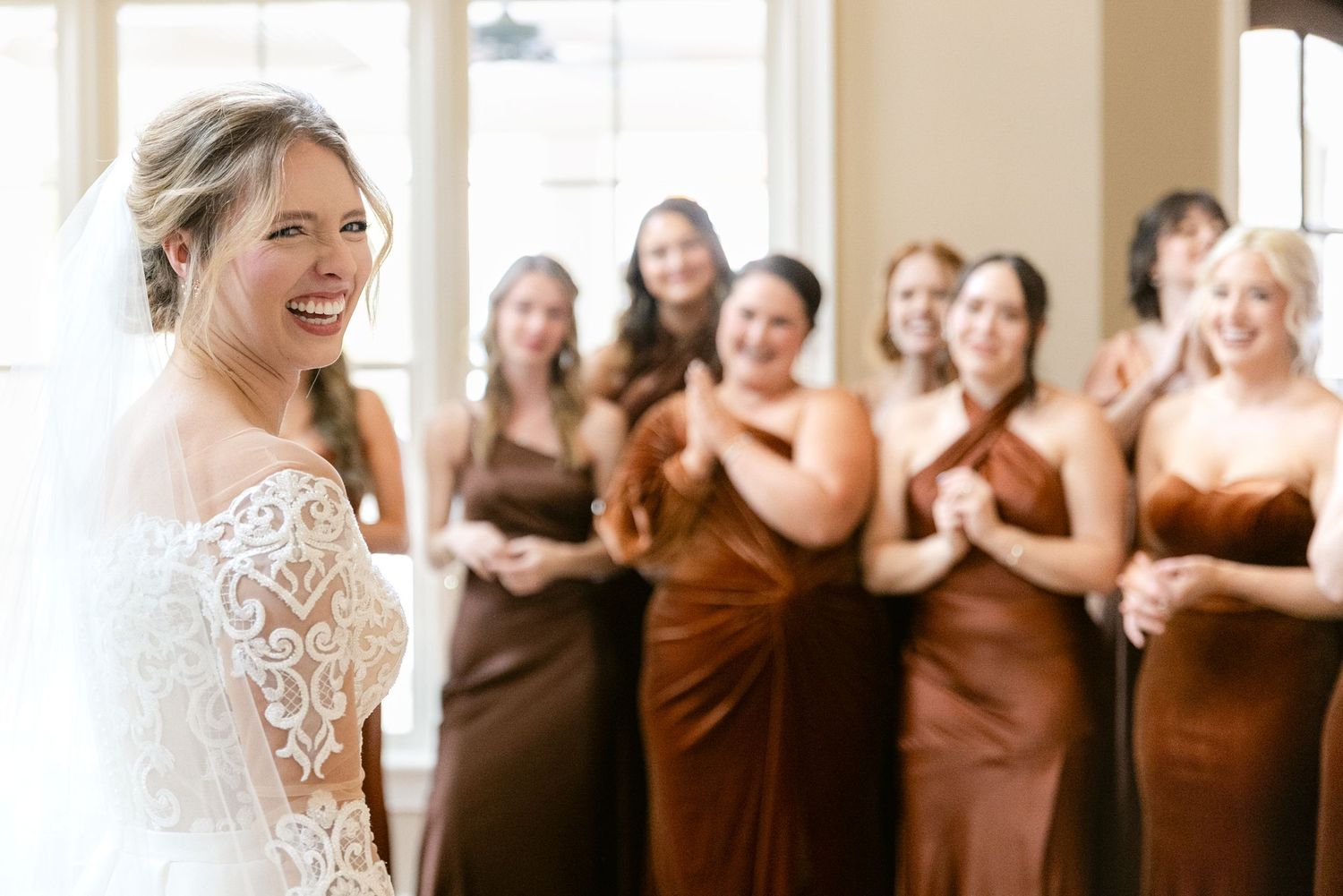 A group of bridesmaids in brown dresses stand together smiling at a wedding celebration.