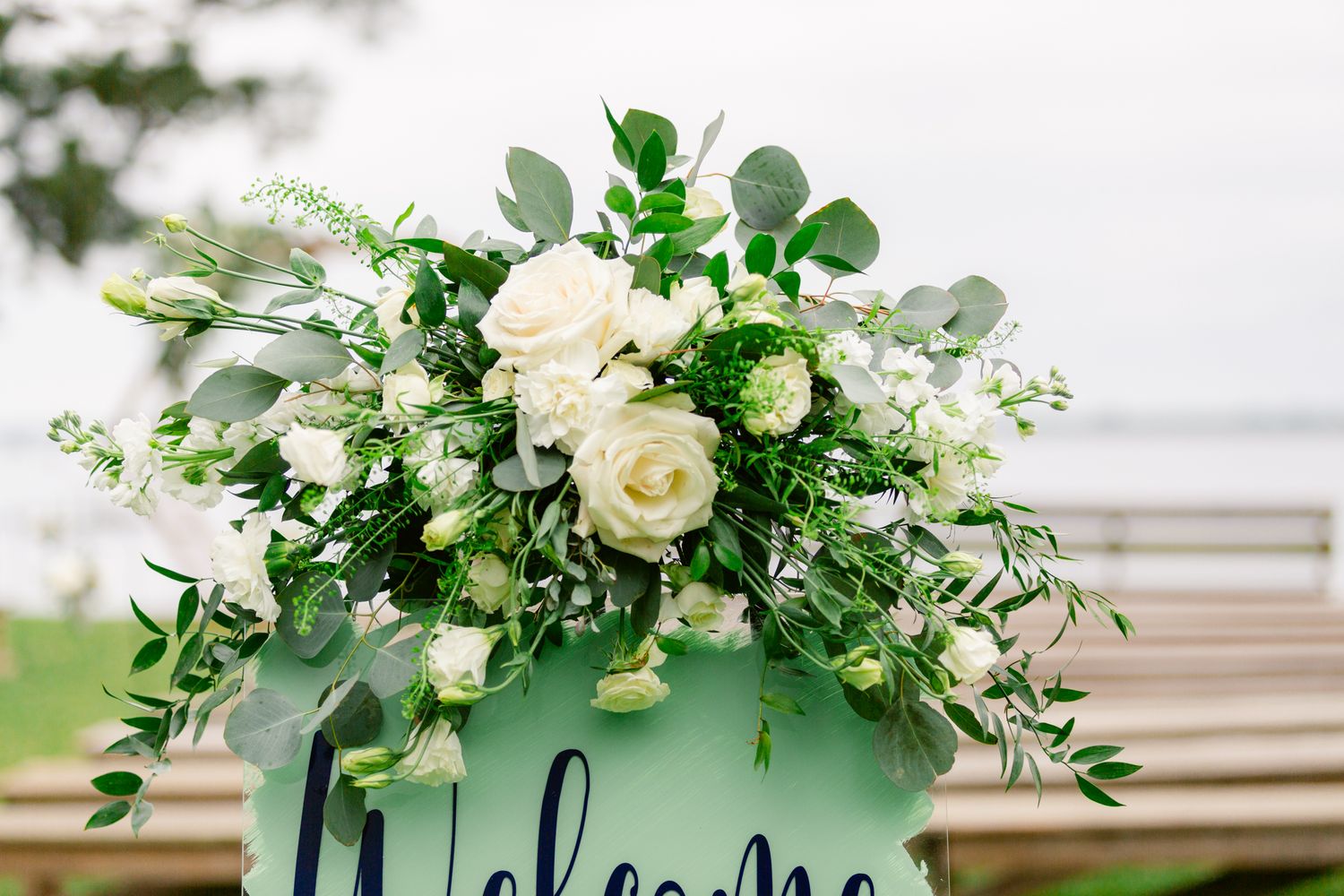 White roses and greenery decorate a rustic wooden ceremony arch at an outdoor wedding venue.