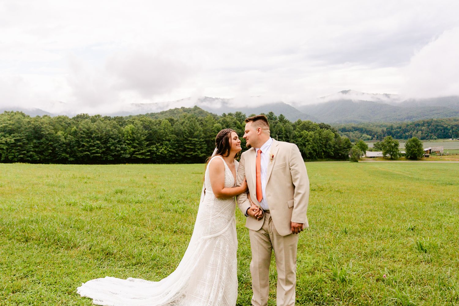 Couple celebrating their wedding in an expansive green field with mountains in the background.