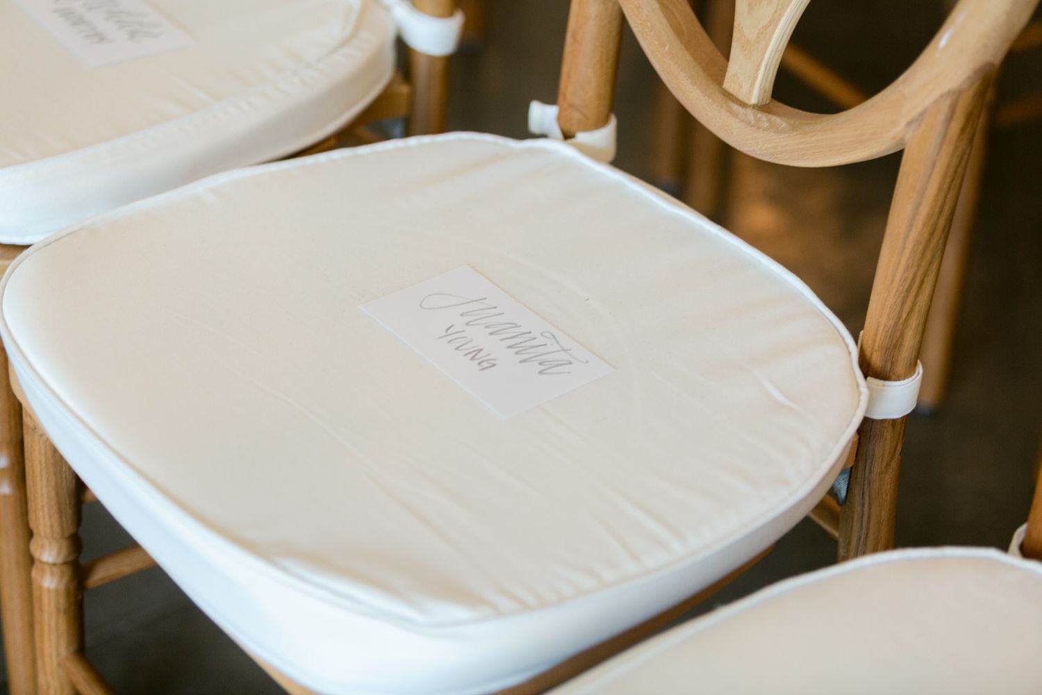 Row of white cushioned chairs with protective plastic covers arranged against a neutral wall.