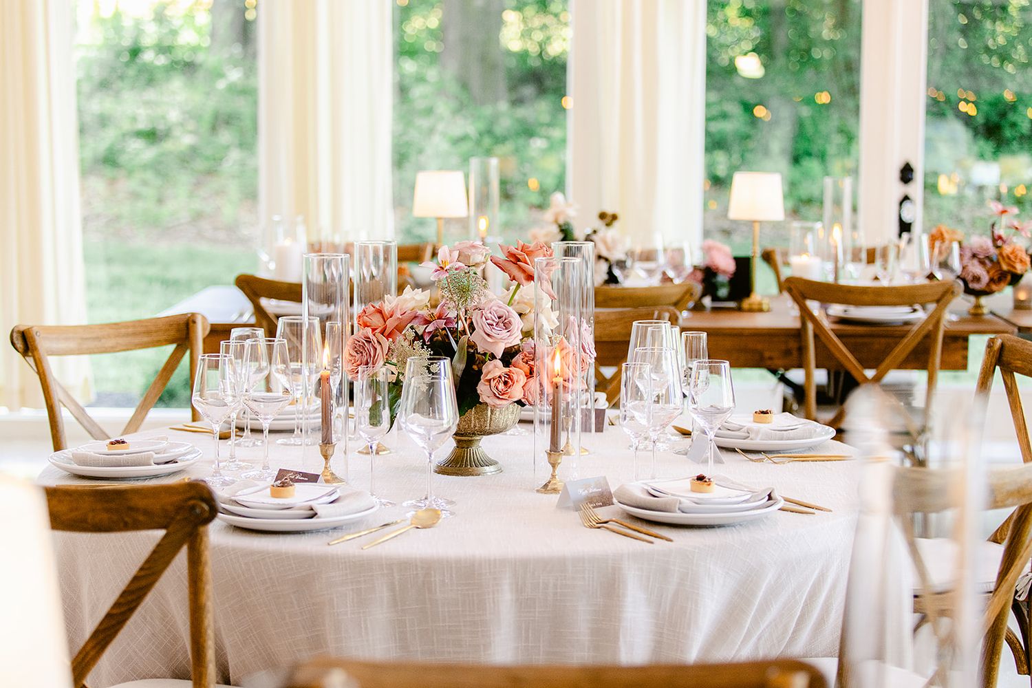 Wedding reception space decorated with round tables, wooden chairs, and soft pink floral arrangements.