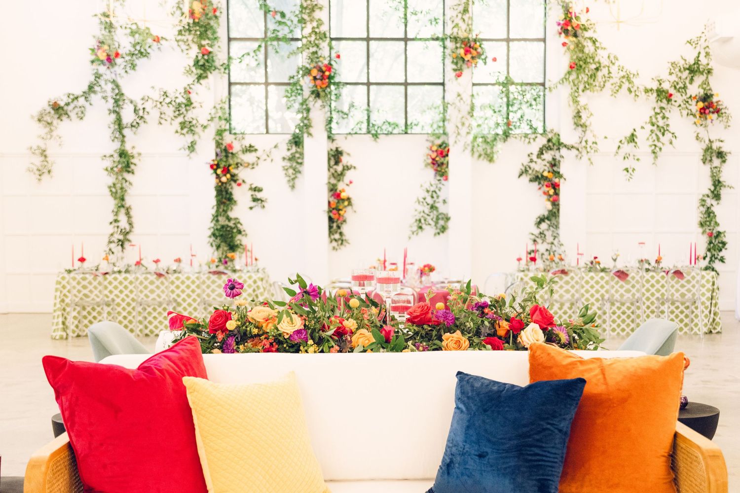 Modern event space decorated with hanging floral arrangements and colorful throw pillows.