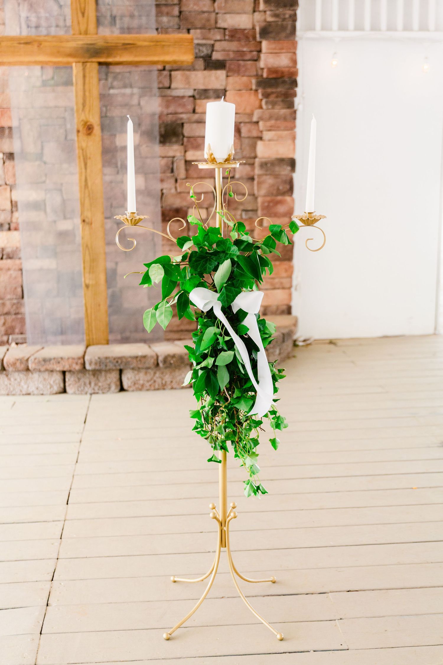 Gold candle holders with greenery arrangements against exposed brick walls in an event space.