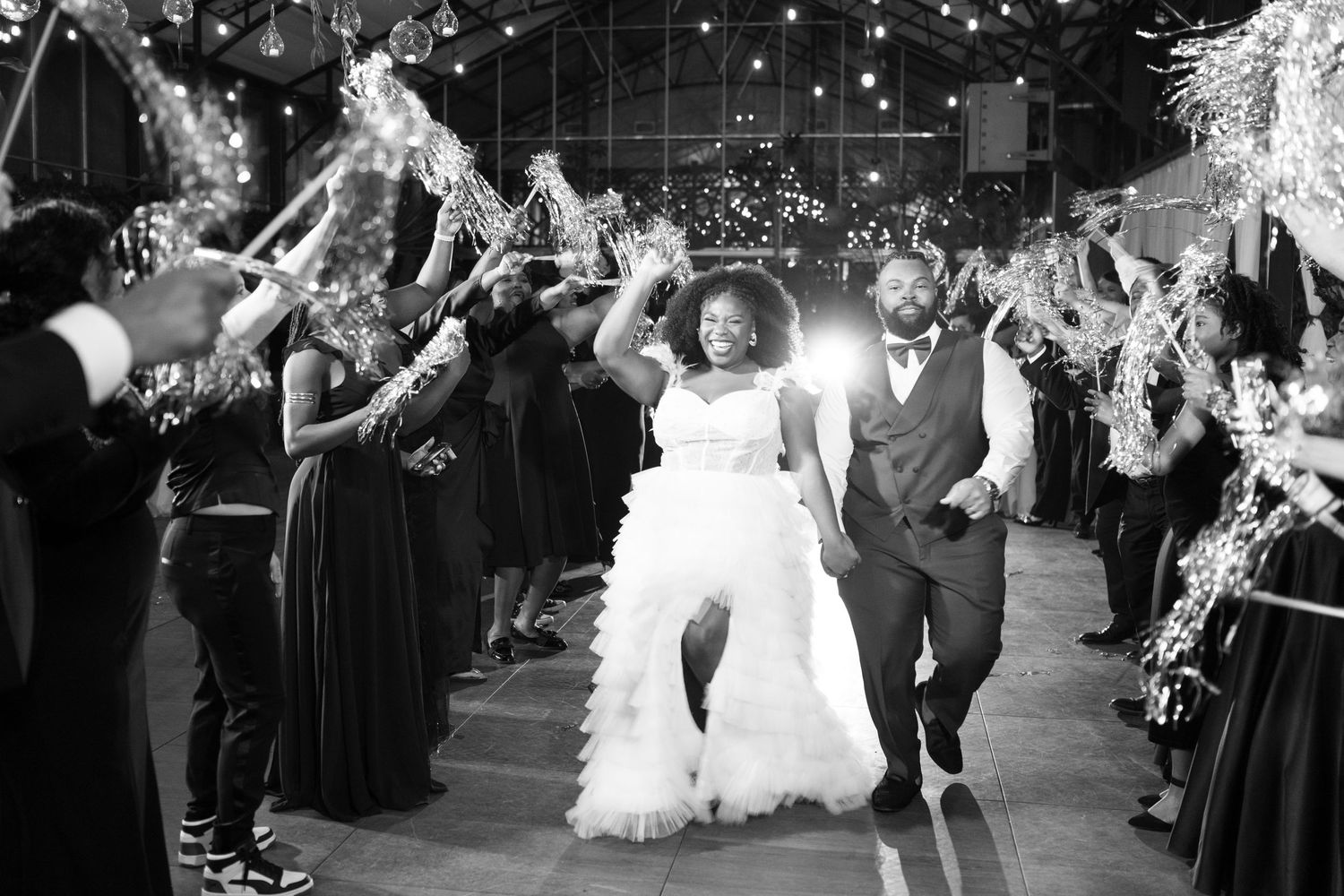 Wedding guests dance and celebrate on a dance floor during an evening reception with twinkling lights overhead.