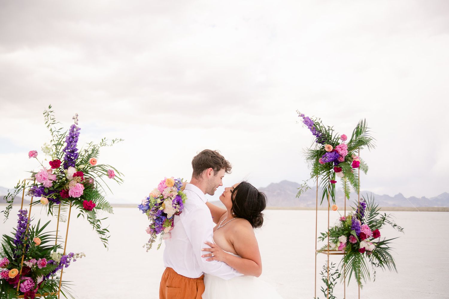 A romantic beach wedding ceremony with floral arrangements in pink and purple against a misty coastal backdrop.