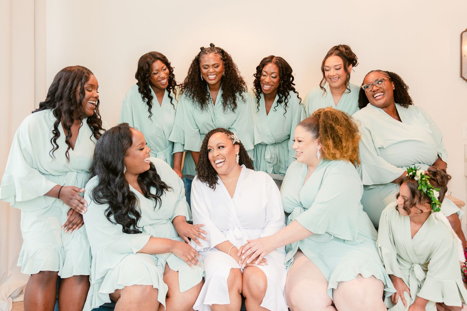 Candid moment of bridal party in mint green robes laughing together.