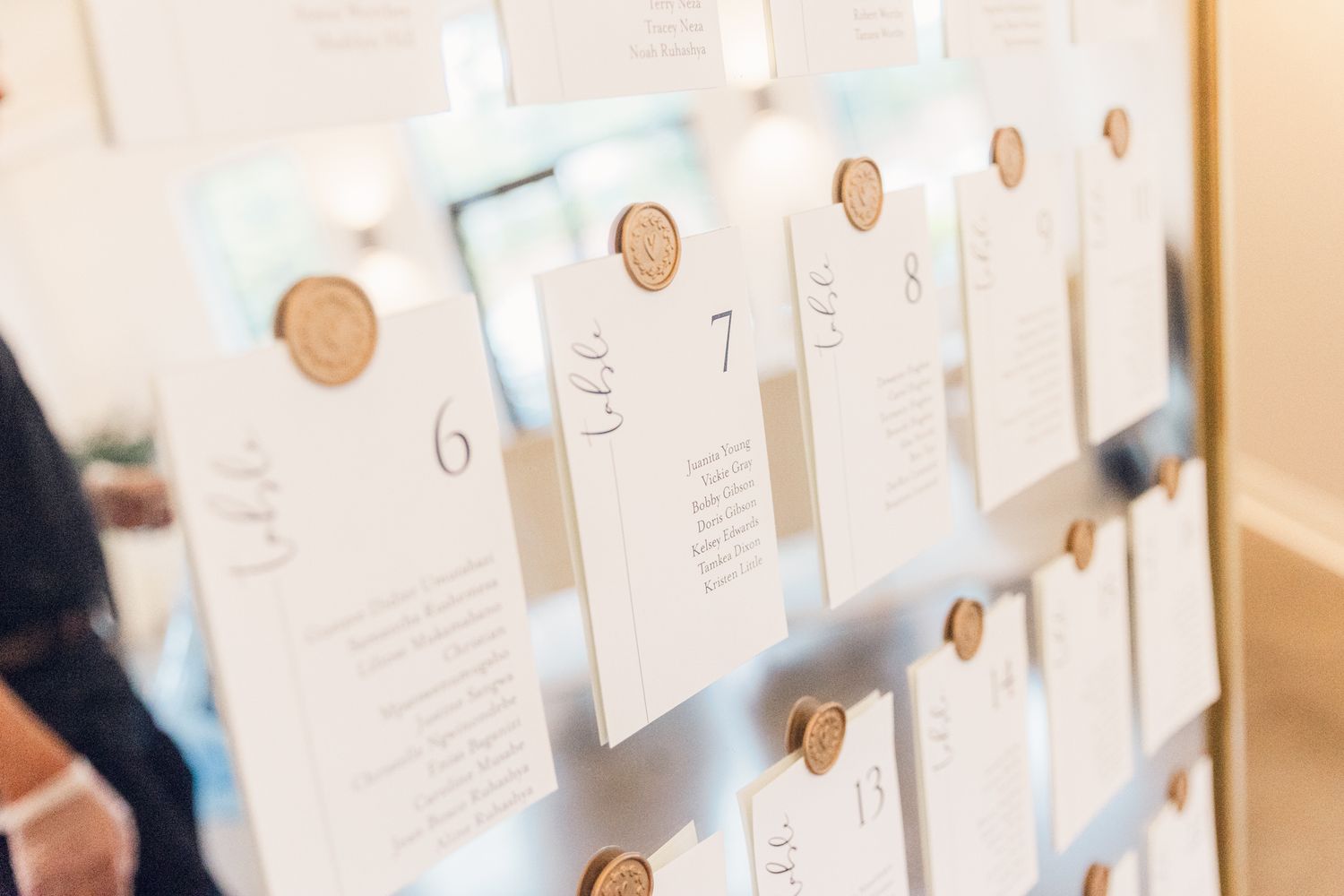 Wedding seating chart cards with wax seals displayed on white strings against a light colored wall.