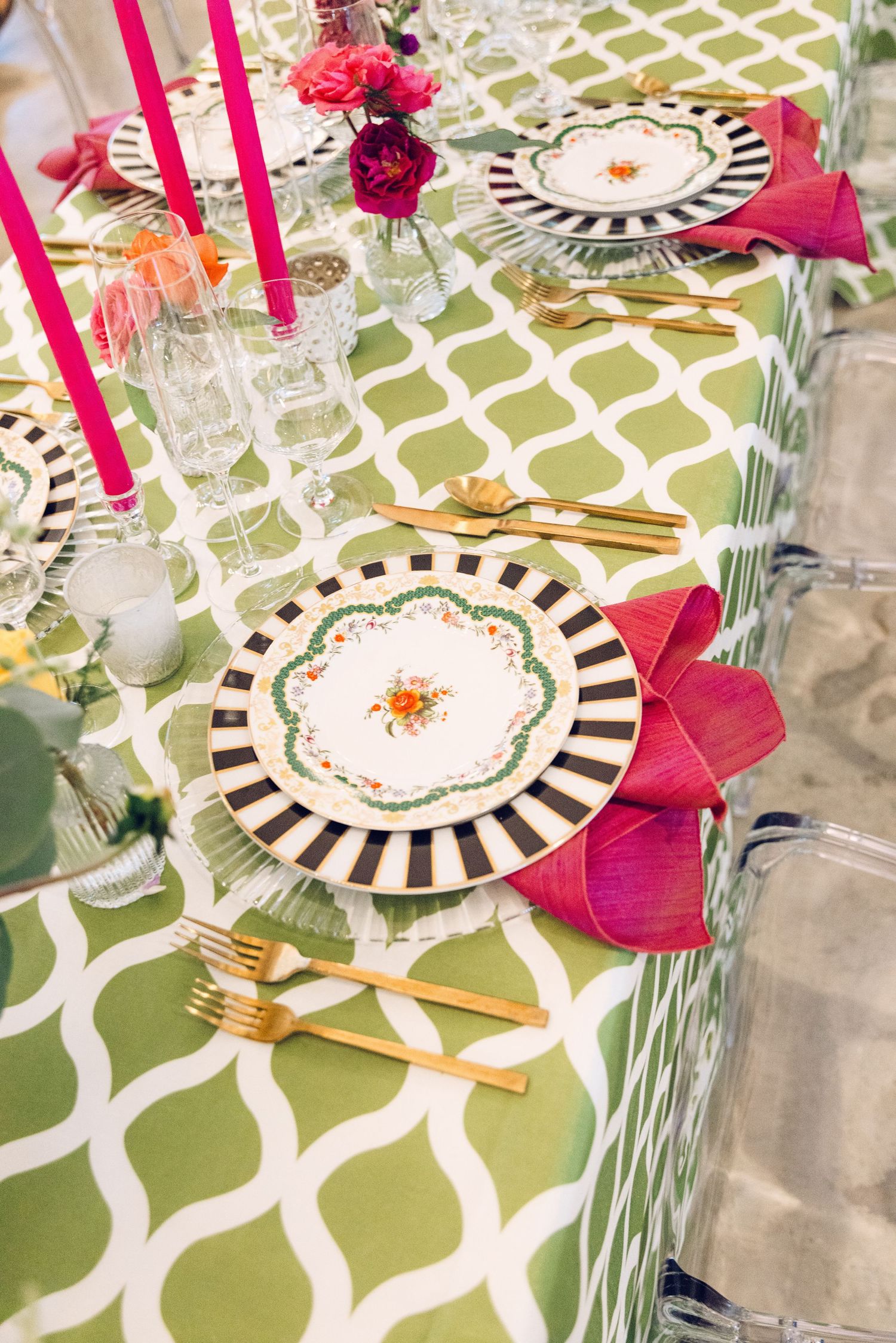 Elegant table setting with green and white patterned tablecloth, striped plates, and pink floral accents.