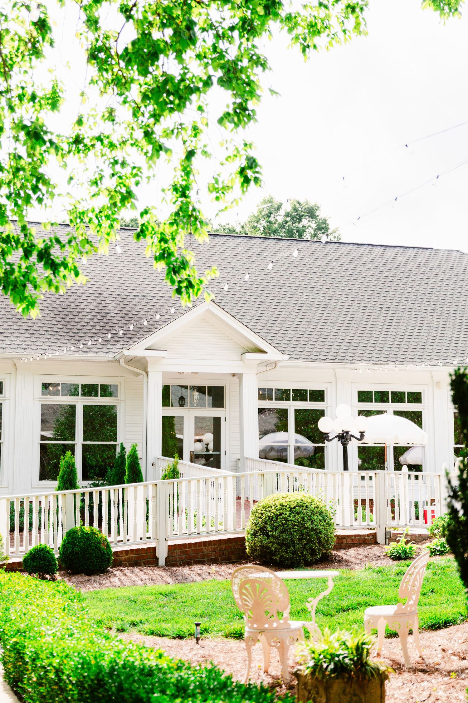 Long white porch with railing and multiple windows overlooking manicured garden with decorative stones.