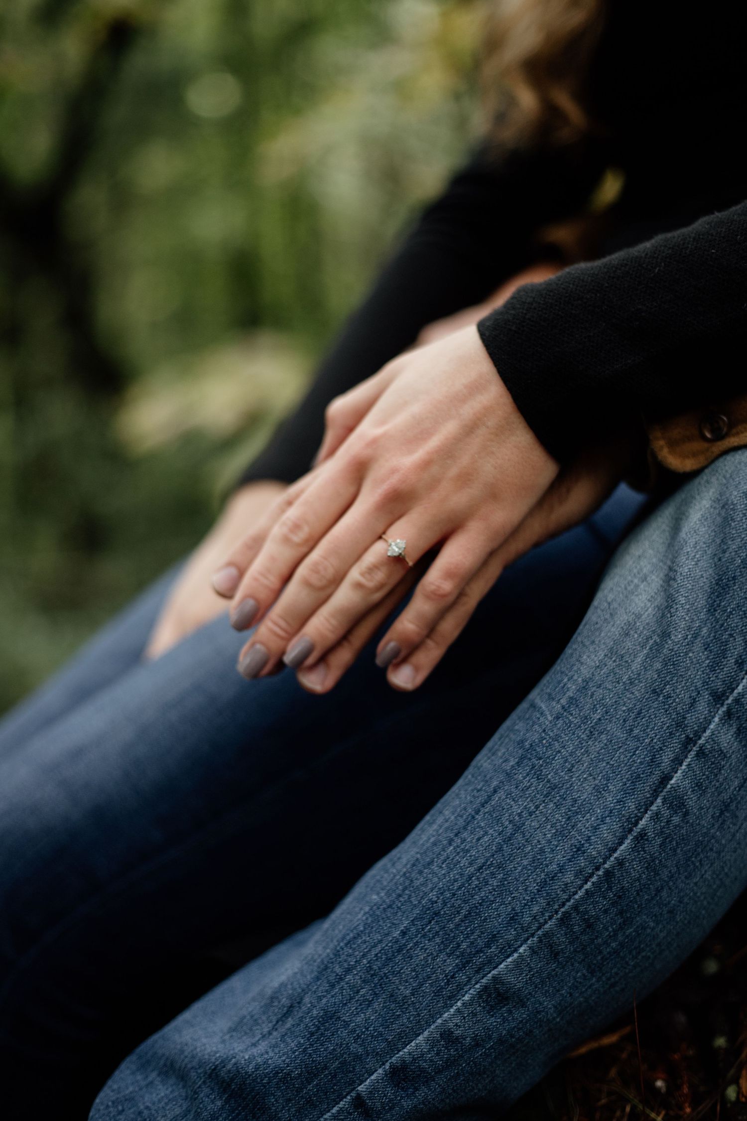 Close-up of hands resting on denim, showing an engagement ring.