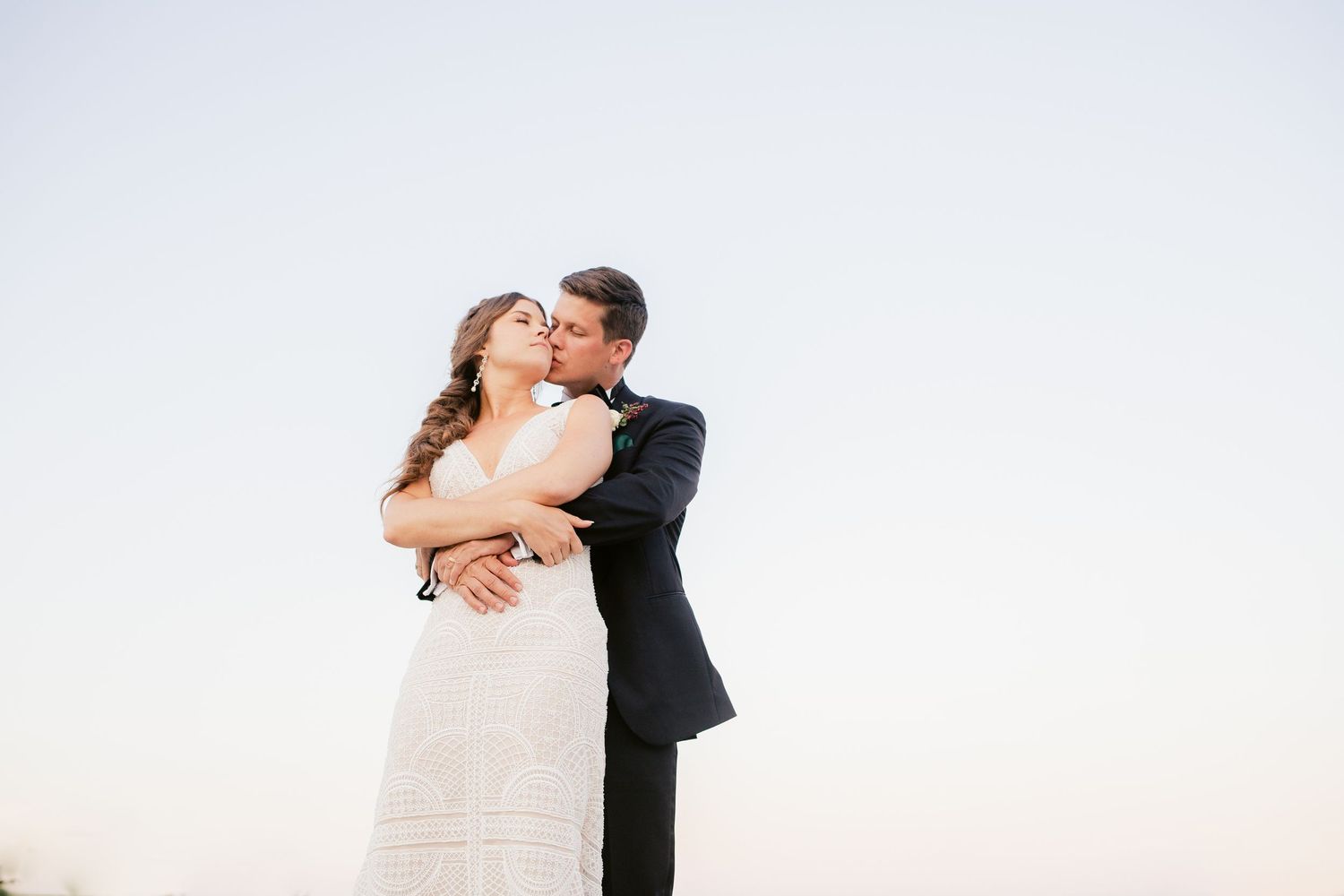 Romantic wedding couple embraces while dancing outdoors during sunset.